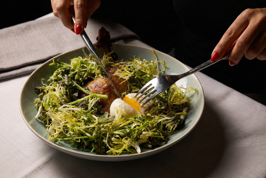 woman with red nails cutting egg ontop of duck confit salad