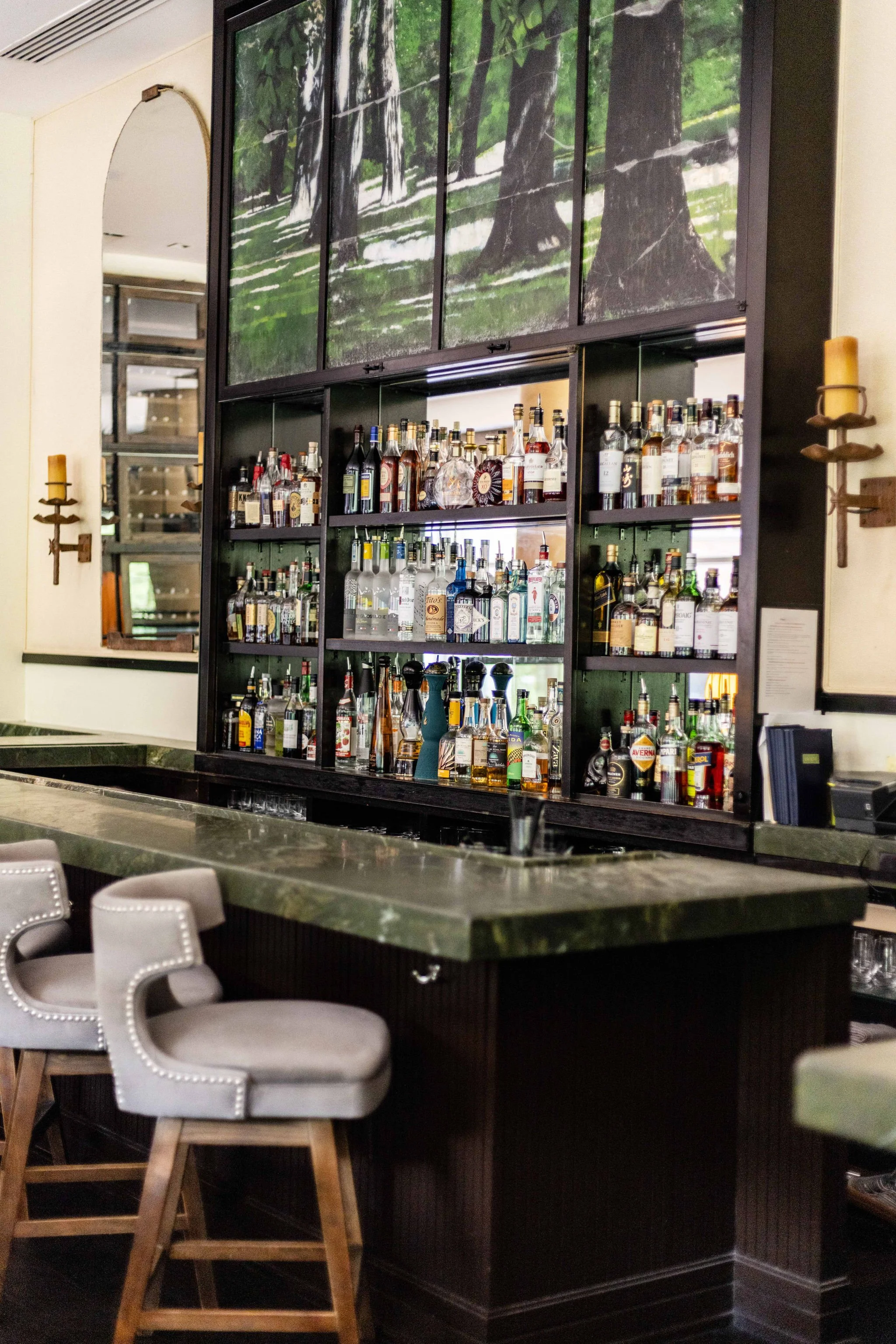 bar interior showing liquor bottle filled shelves and gray bar chairs. image of forest above bar