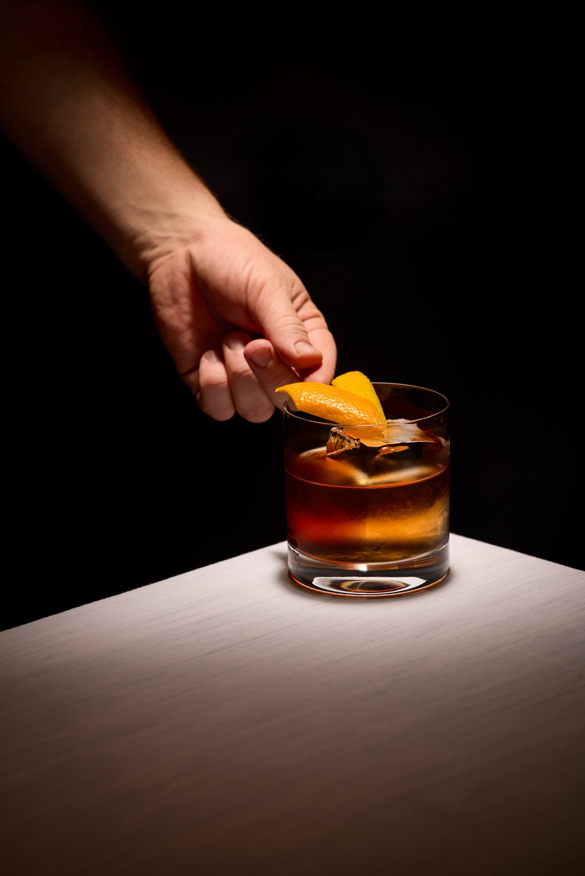 hand placing orange peel garnish on a negroni cocktail