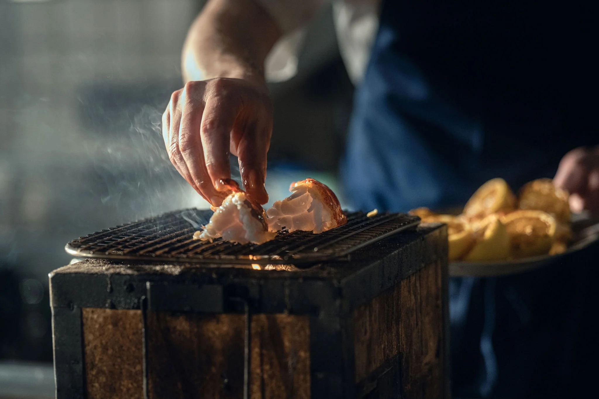 Person grilling lobster on a barbecue with lemon wedges in the background.