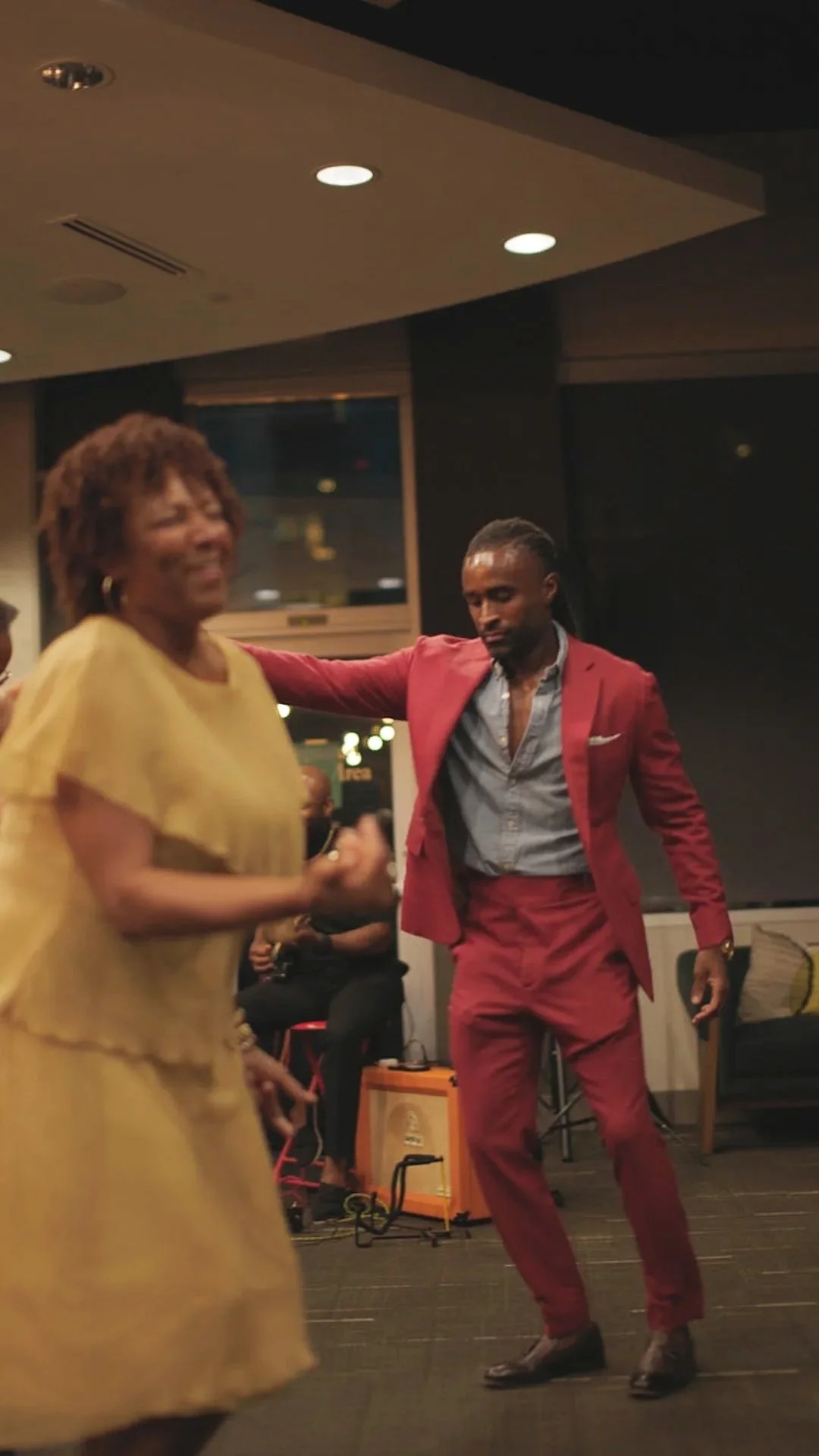 Two people dancing indoors, a woman in a yellow dress and a man in a red suit