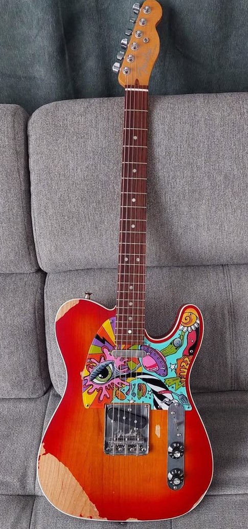 An electric guitar with a colorful, artistic design on the body, featuring abstract and eye imagery, placed on a gray sofa.