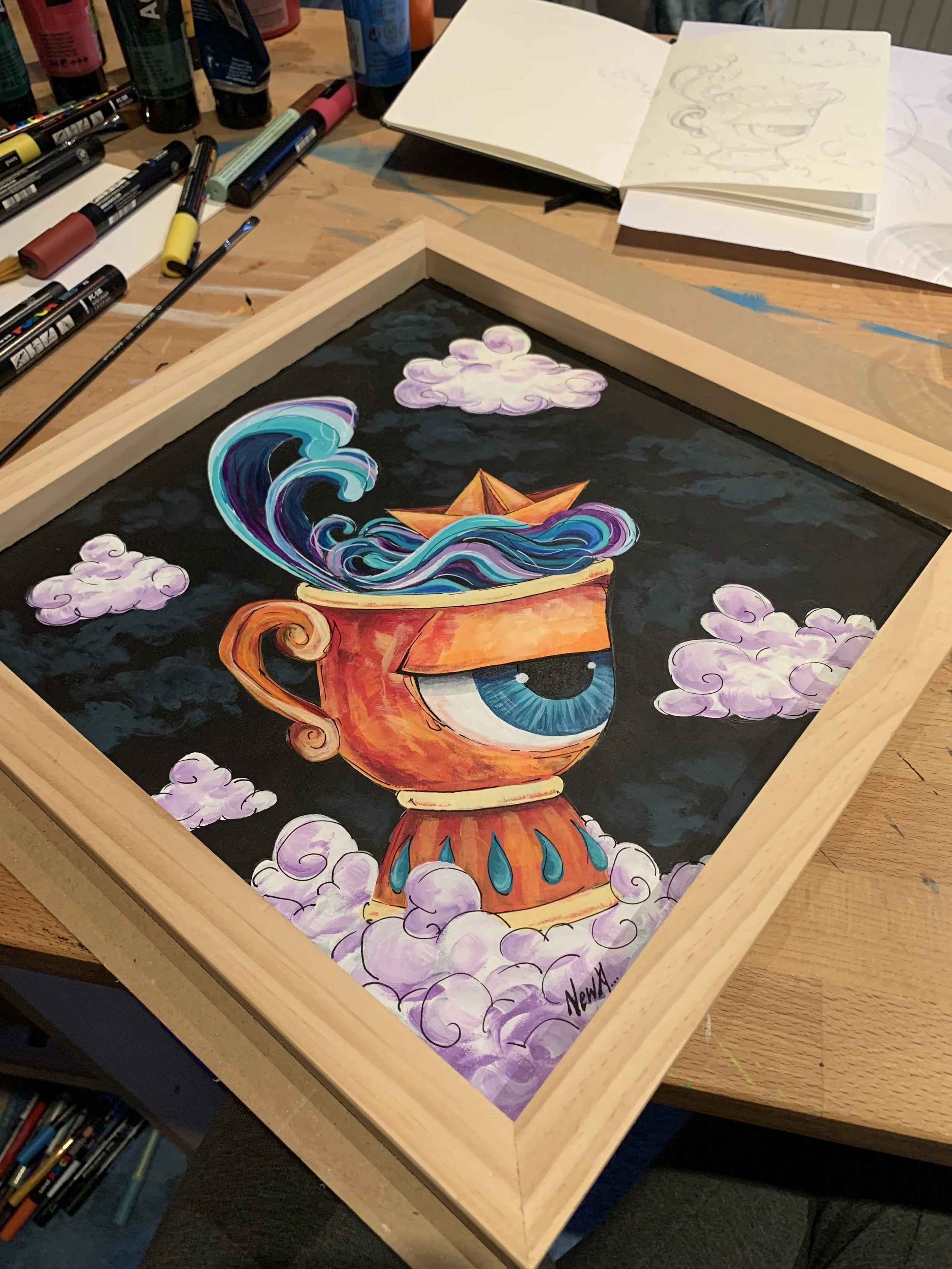 A colorful painting of a coffee cup with an eye on it, with ocean waves and clouds emerging from the cup, inside a wooden frame.