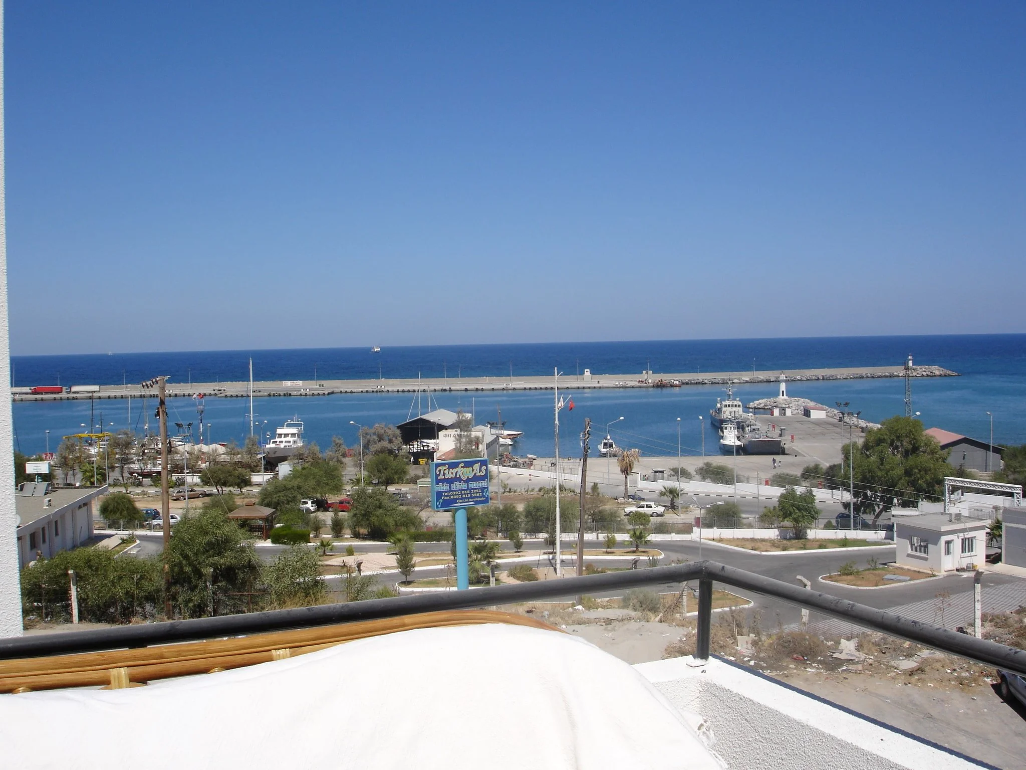 View of a marina with boats, a lighthouse, and a harbor breakwater extending into the ocean on a clear, sunny day.