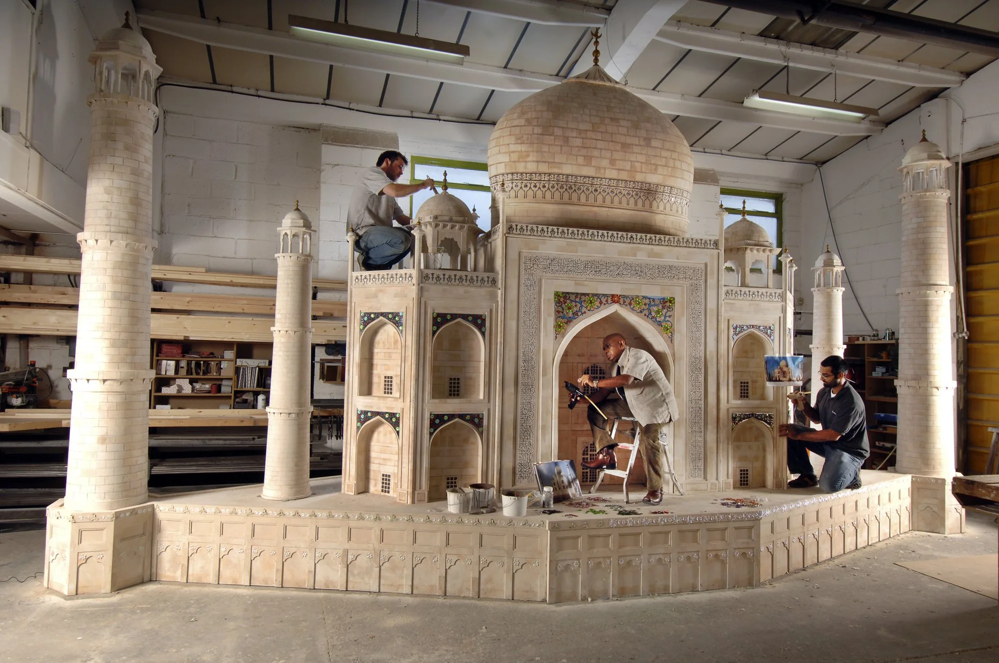 People working on constructing a detailed scale model of a mosque with domes and minarets in an indoor workshop.