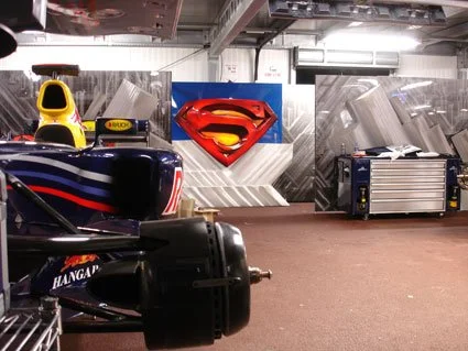 Garage with racing car, Supergirl logo, and Superman logo decor.