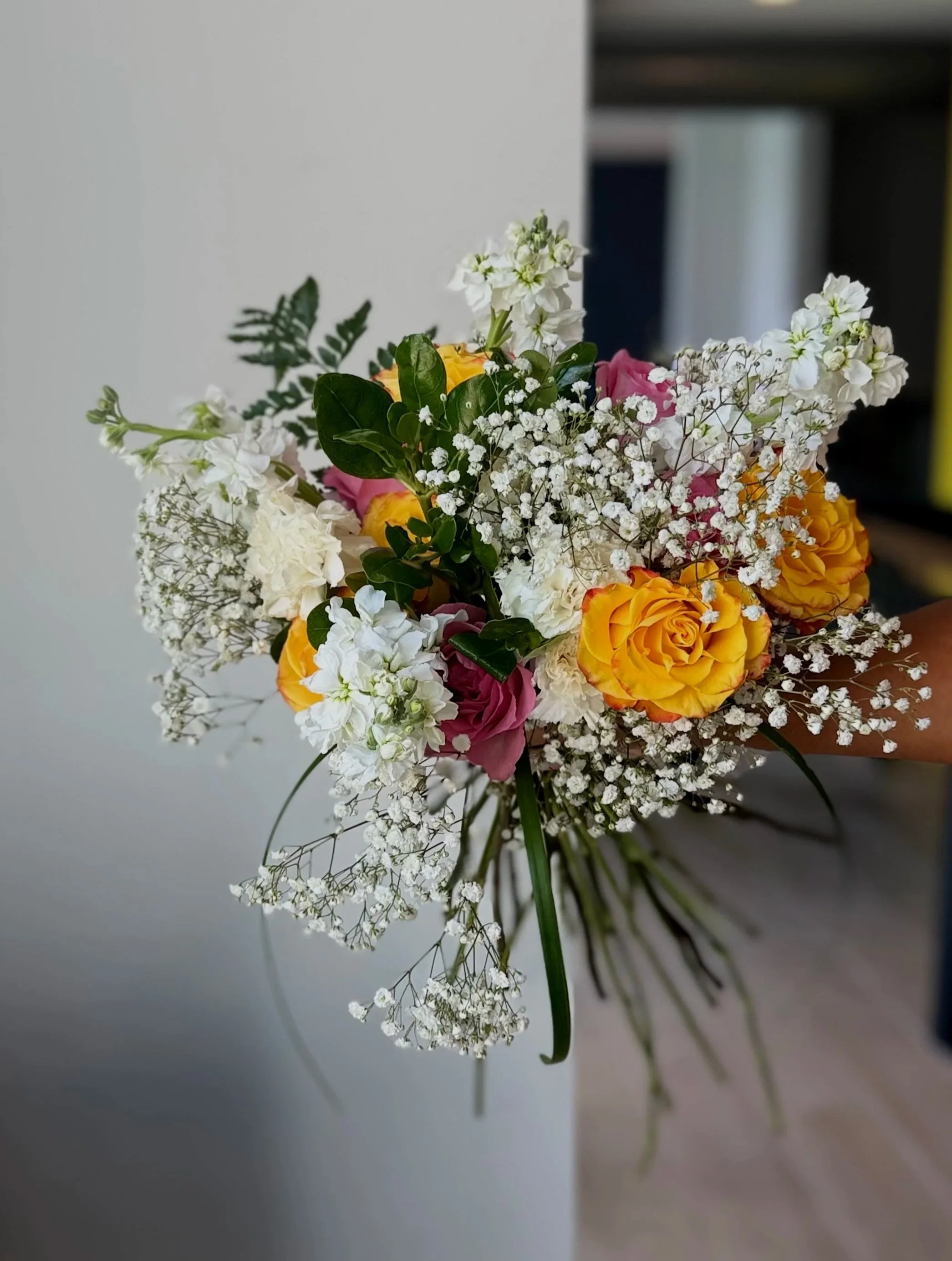 Bouquet of white, yellow, pink, and orange roses with white baby's breath and greenery.