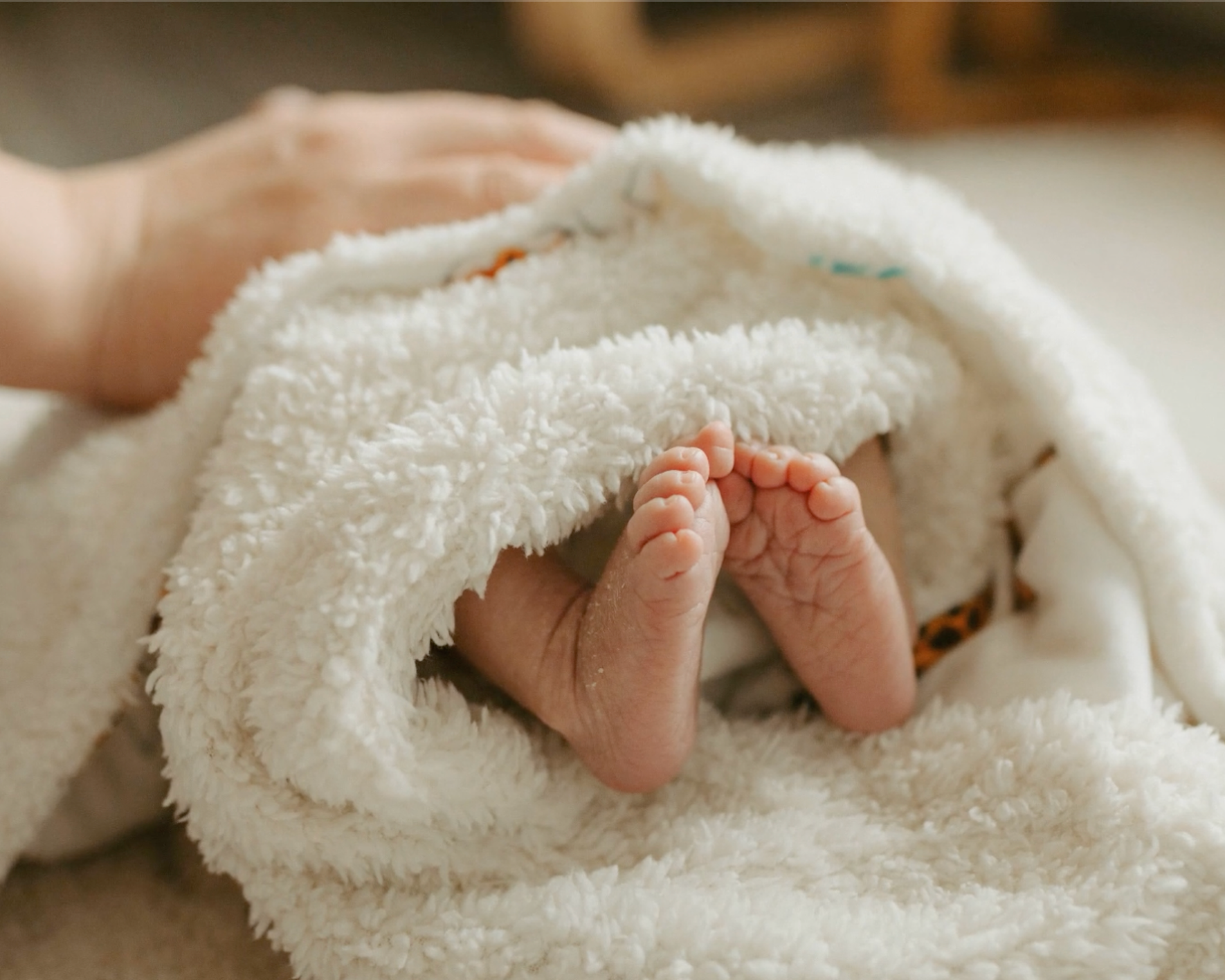 Newborn baby feet emerge from a white swaddling.