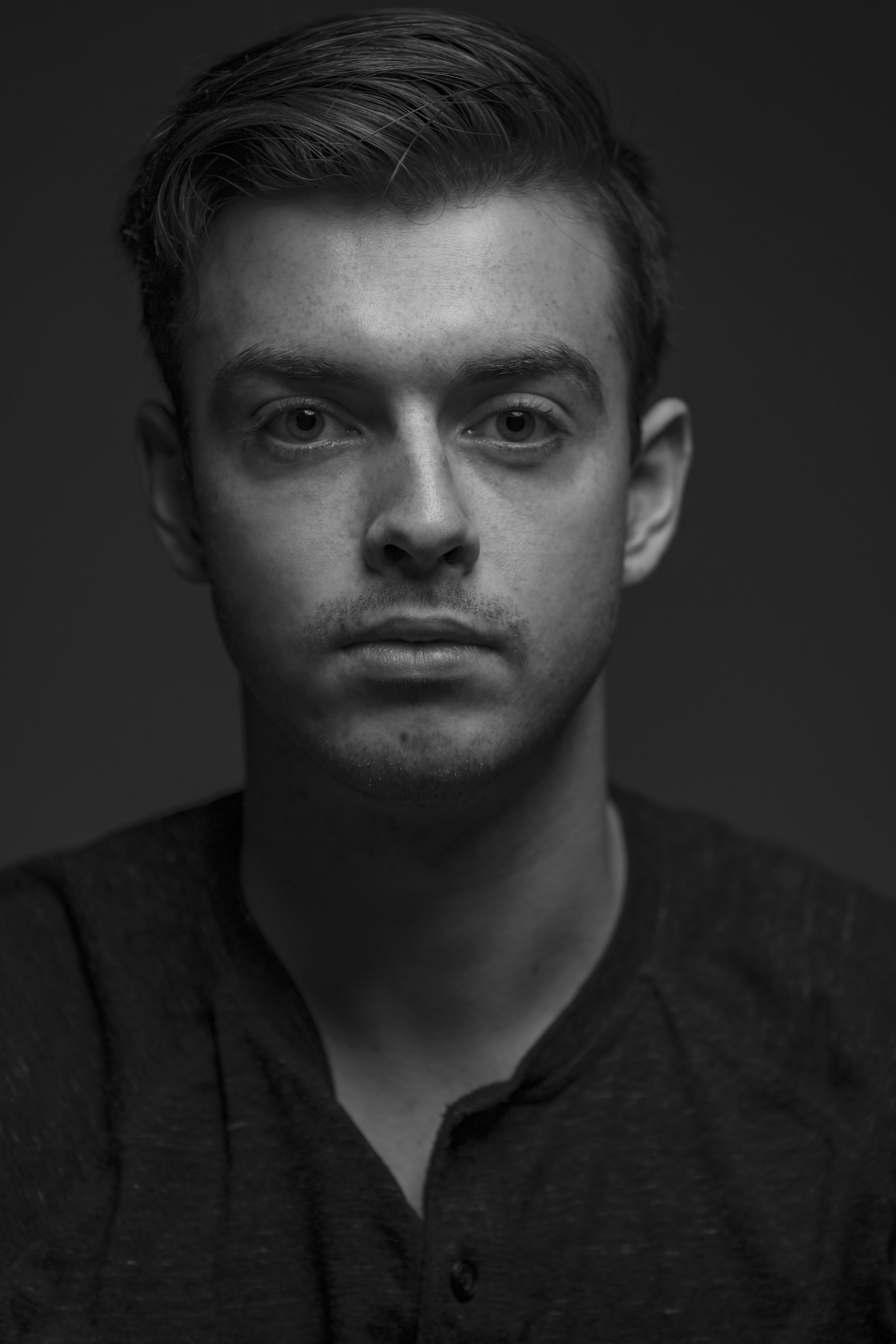 Black and white close-up portrait of a young man with short hair, serious expression, and wearing a dark shirt. BoldVision Studios