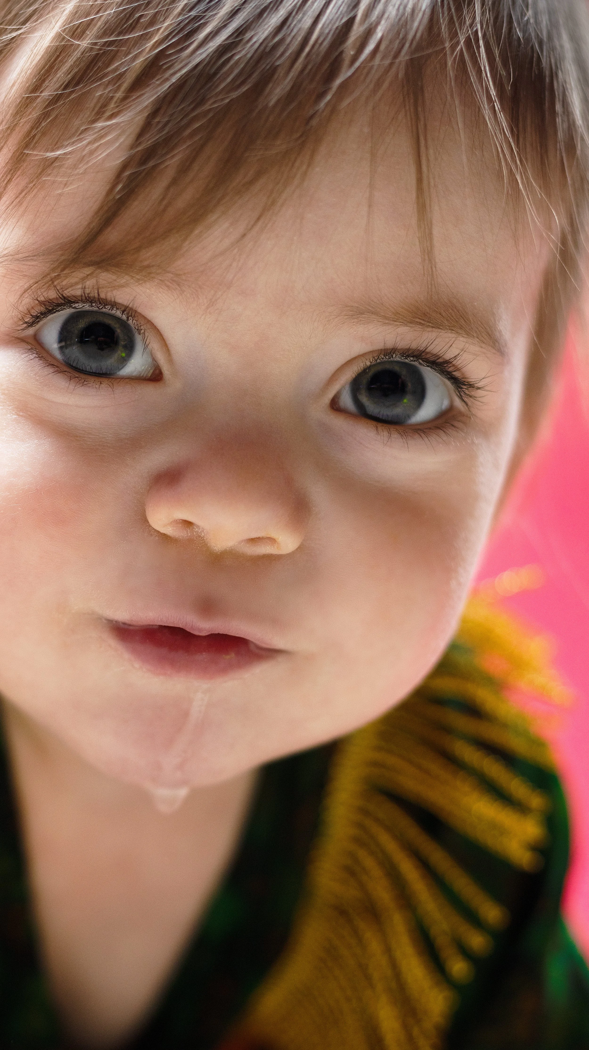Close-up of a young child's face with big blue eyes, light skin, brown hair, and a slight smile, wearing a colorful sweater. BoldVision Studios