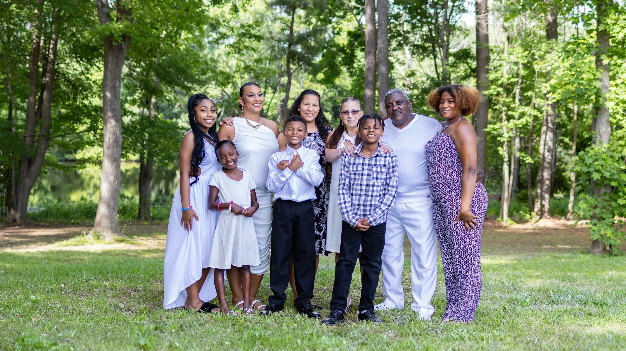 A multigenerational African American family standing together in a forested park, smiling at the camera.