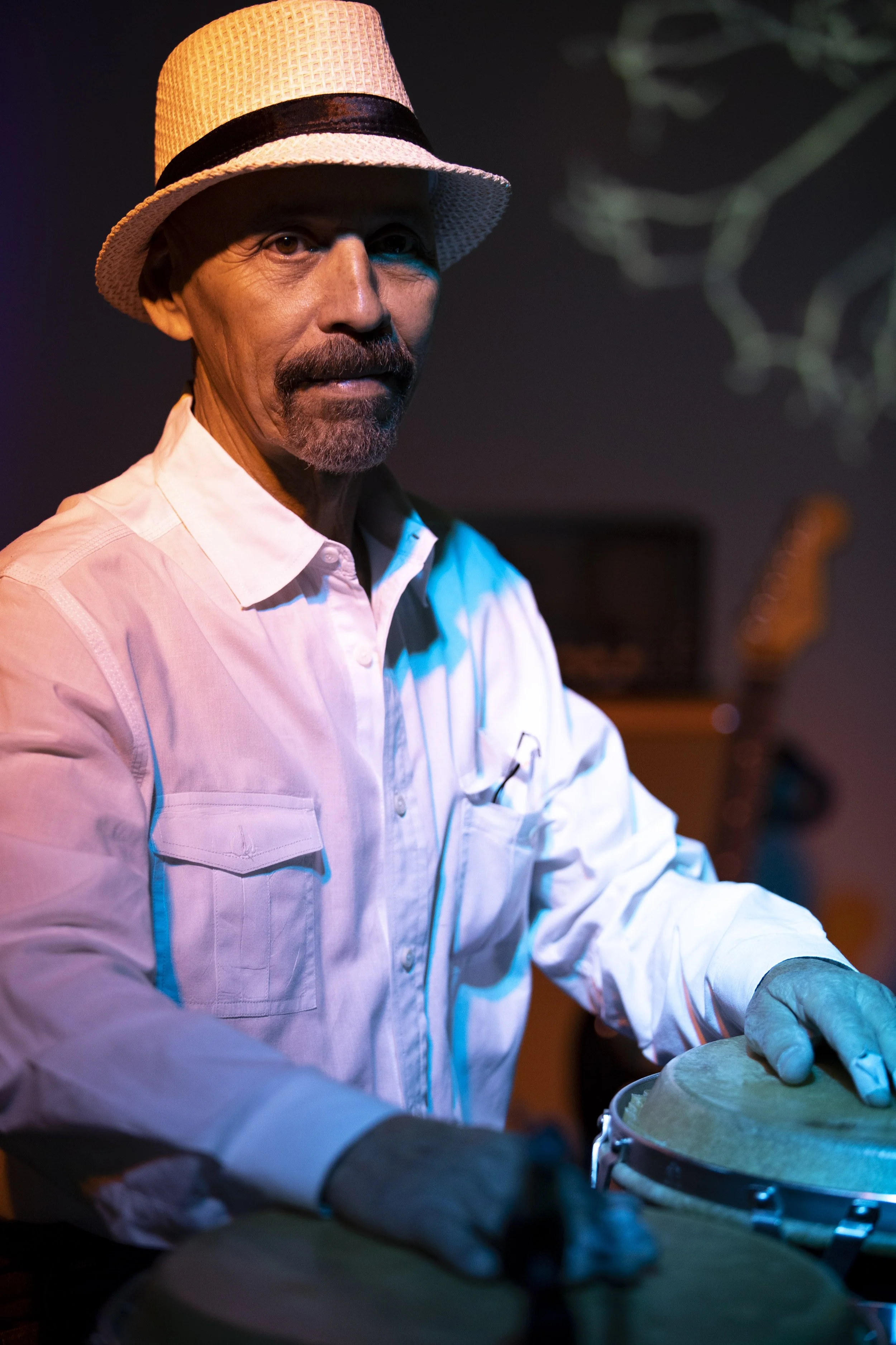 A man wearing a white shirt, a straw fedora, and white gloves playing conga drums. BoldVision Studios