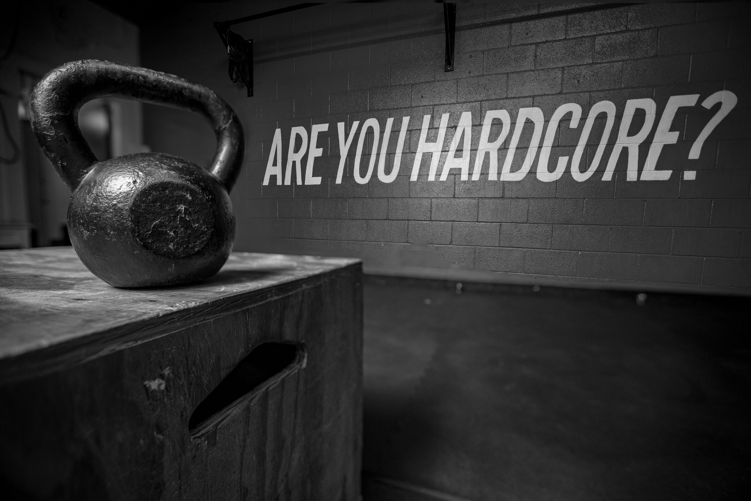 A black kettlebell on a wooden box in a gym with a sign on the wall that reads, "ARE YOU HARDCORE?" BoldVision Studios
