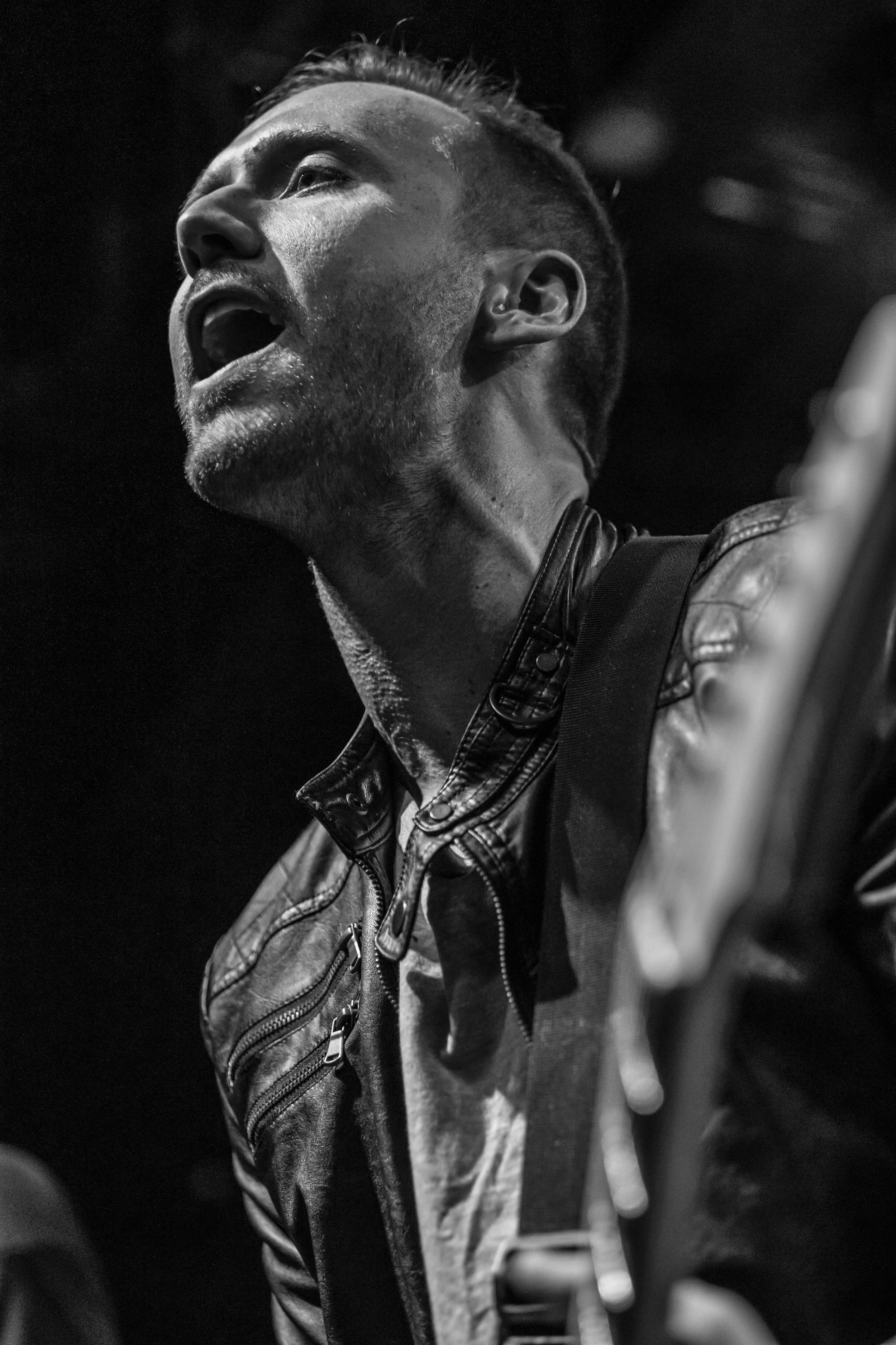 Close-up of a man singing passionately, wearing a leather jacket and guitar strap, in black and white. BoldVision Studios
