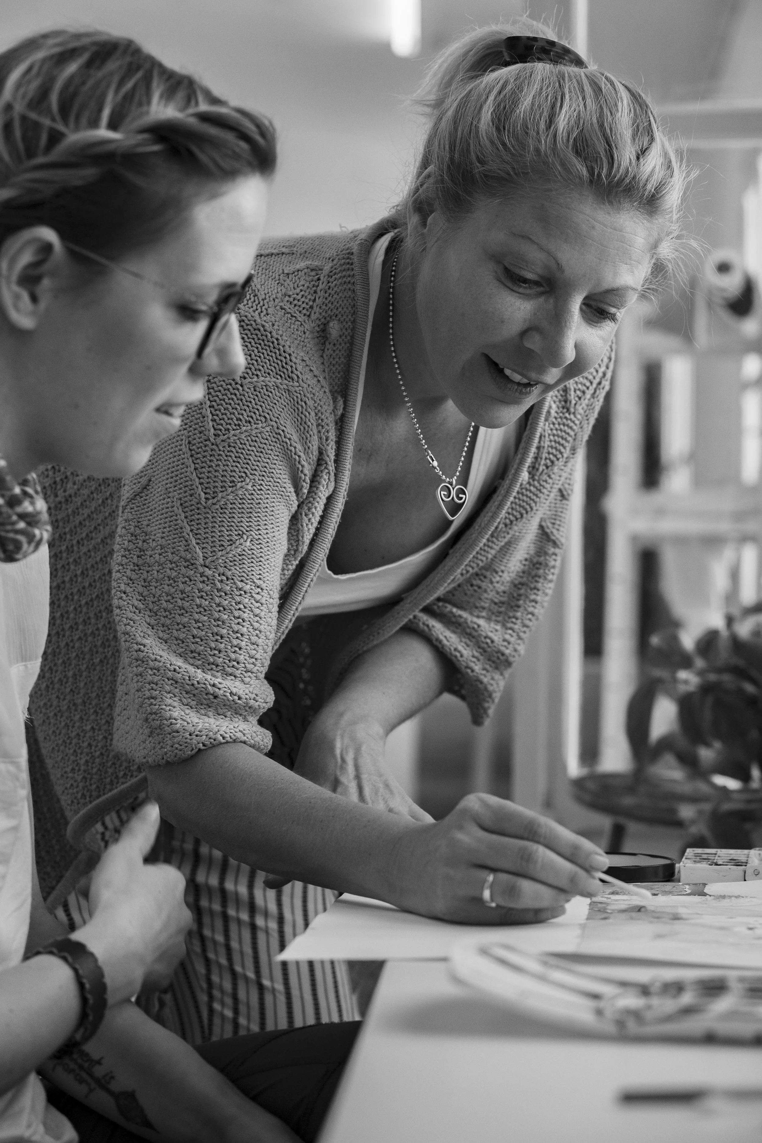 Two women collaborating at a table, with one gesturing towards the paper they are working on. BoldVision Studios