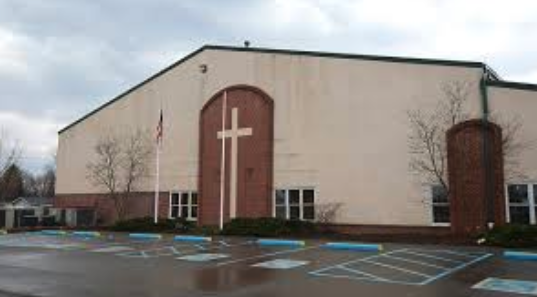 A church building with a large cross on its front, surrounded by parking spaces and a cloudy sky.