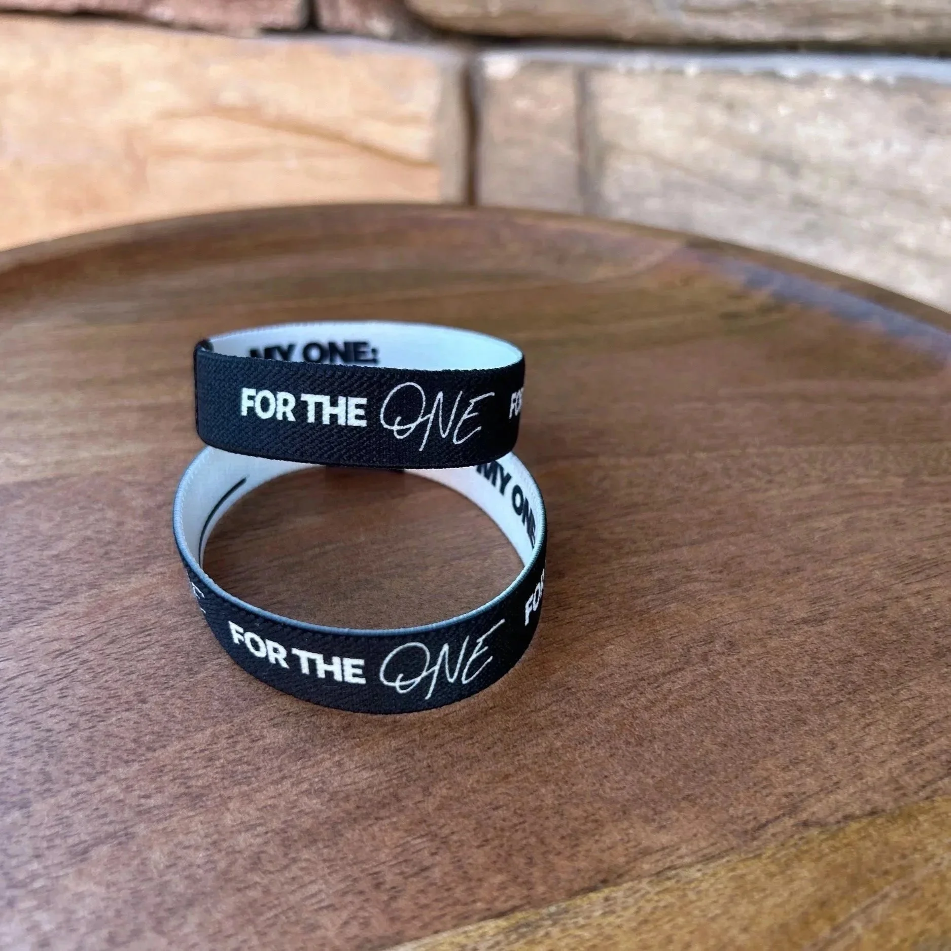 Black silicone wristband with white text reading 'FOR THE ONE' on a wooden surface.