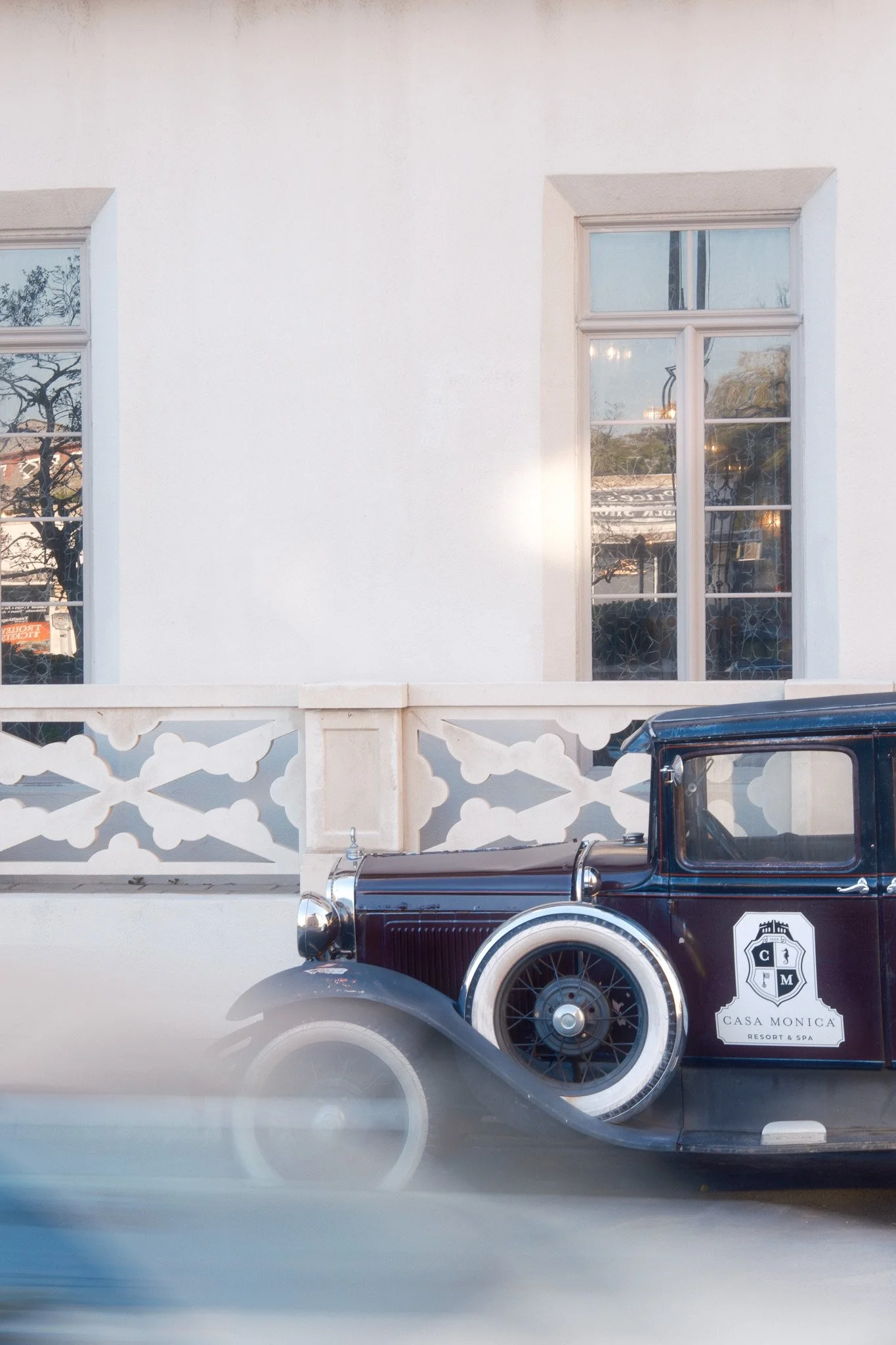 An antique car with a logo that says Casa Monica Resort & Spa parked in front of a white building with large windows.
