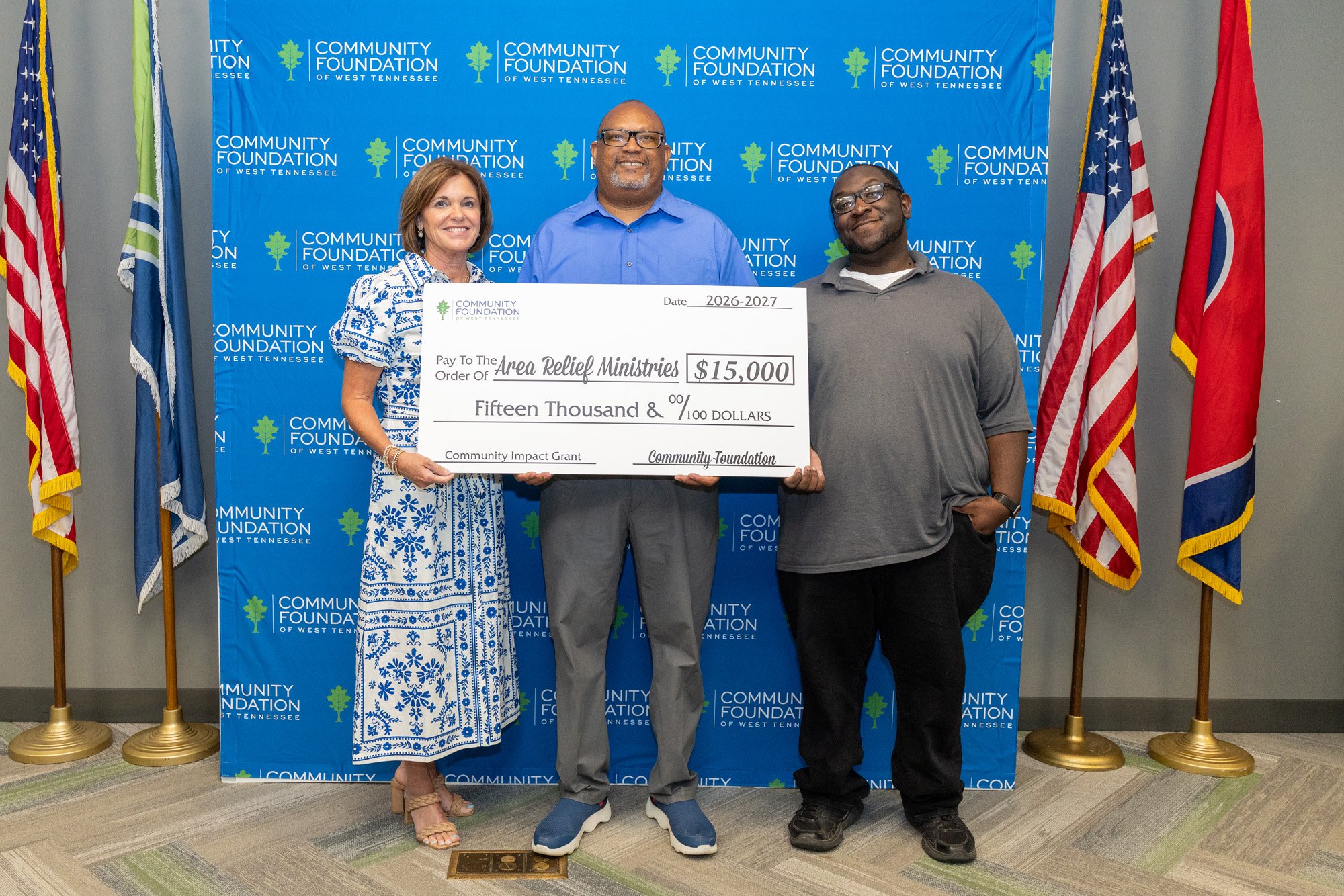 Three people holding a large check for $15,000 made out to Area Relief Ministries, standing in front of a blue backdrop with logos of Community Foundation of West Tennessee.