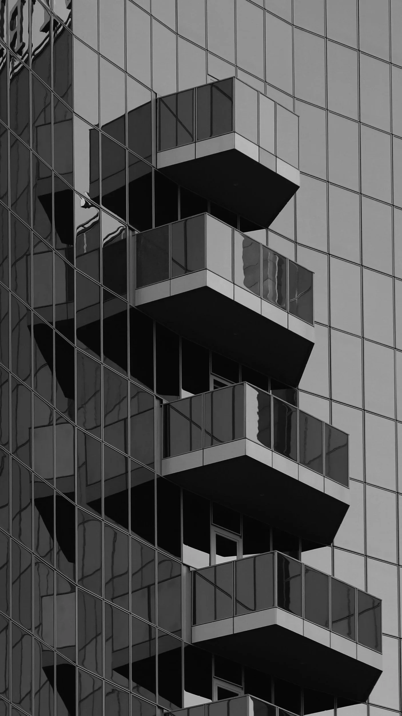 A black and white photo of a modern glass building with multiple balconies on a high-rise structure.