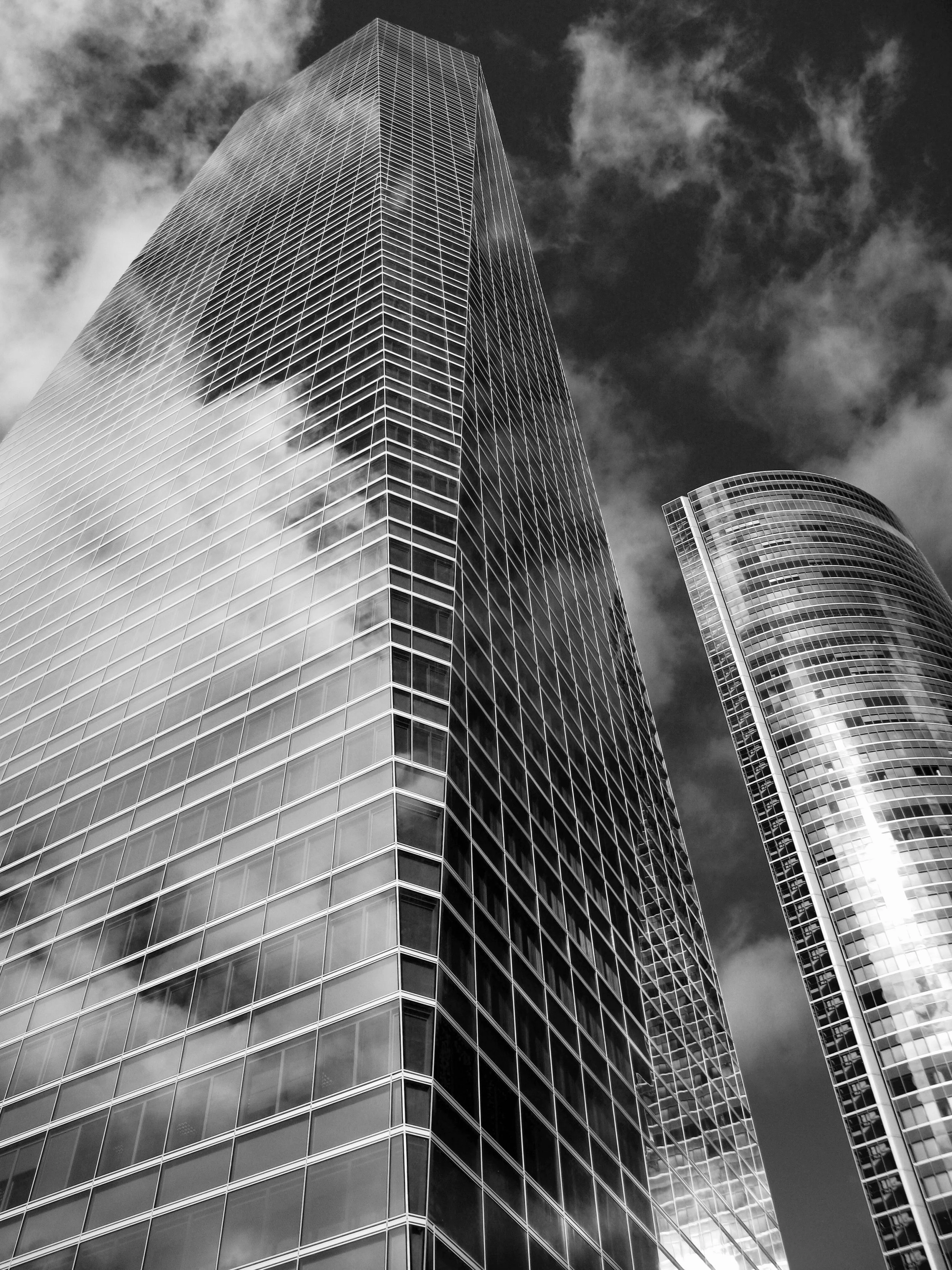 Low-angle view of modern skyscrapers with glass facades reflecting clouds in the sky.