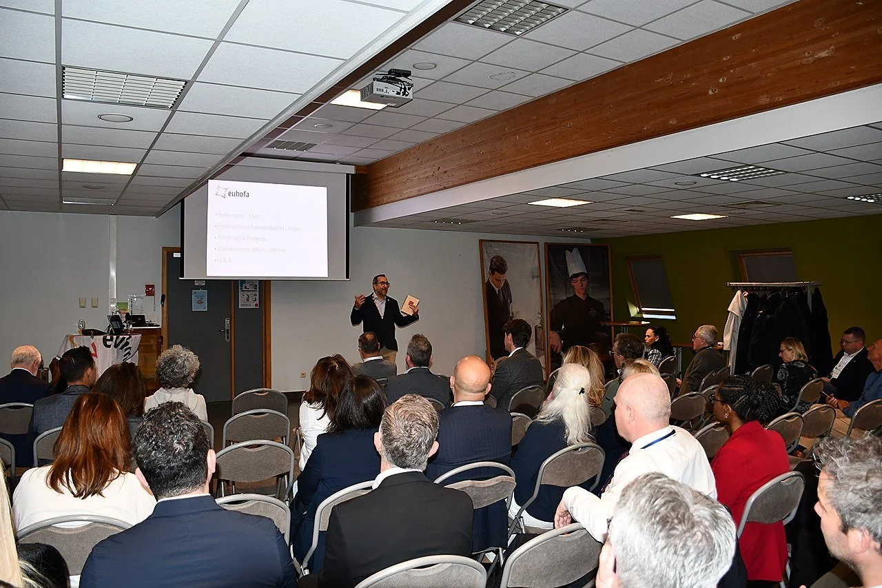 A speaker giving a presentation to an audience in a conference room with a projection screen displaying a presentation slide at EUHOFA Congress..