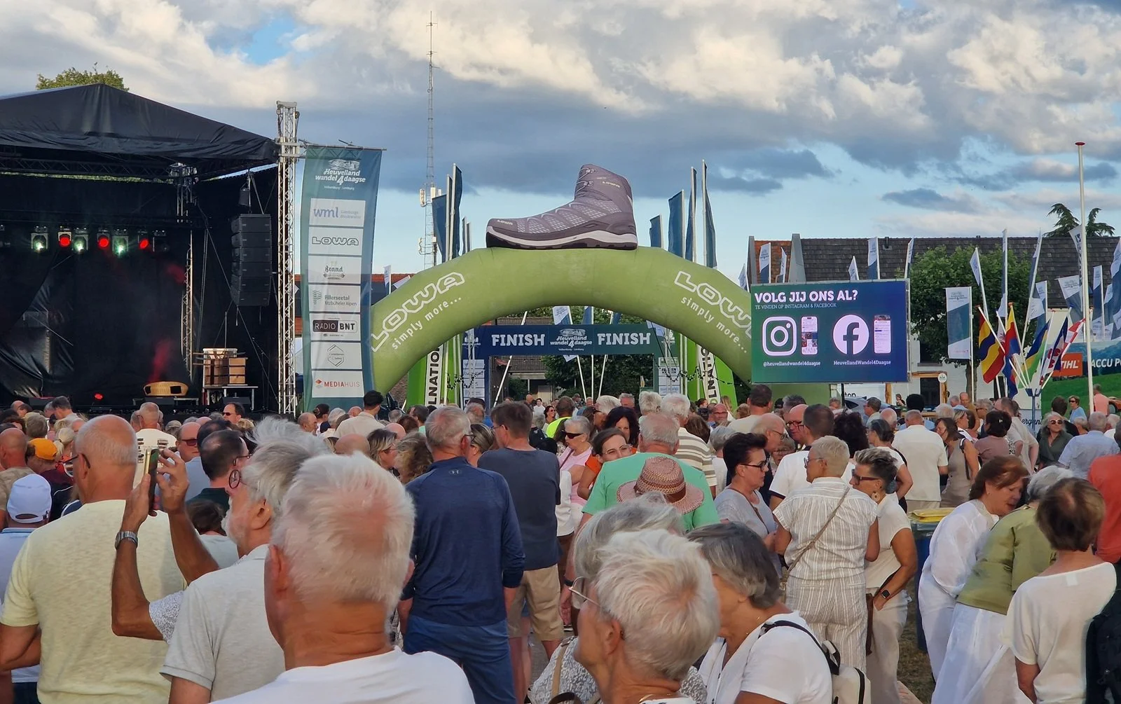 Hiking festival terrain with podium, big video wall and inflatable arch together with many hikers.