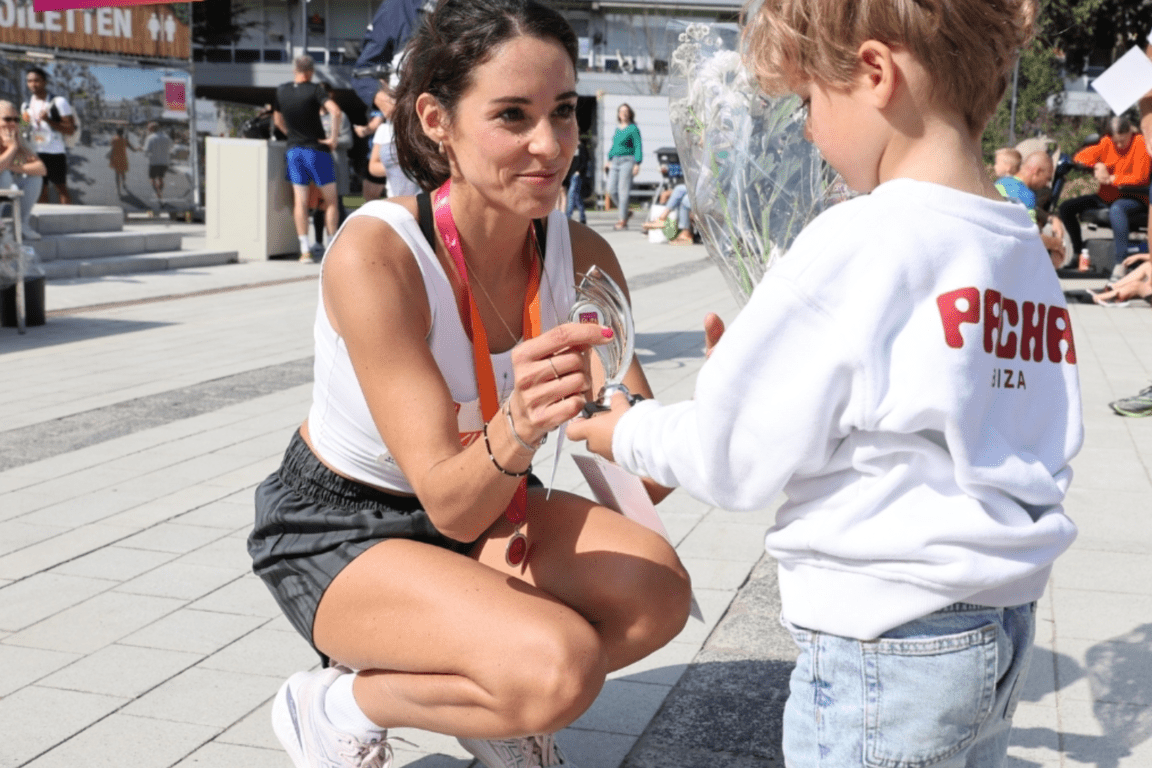 Female runner showing her medal to her child after finishing the event.