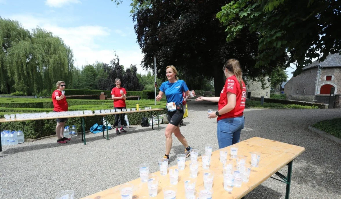 Runners taking water at a refreshment point in a park near a historic castle.
