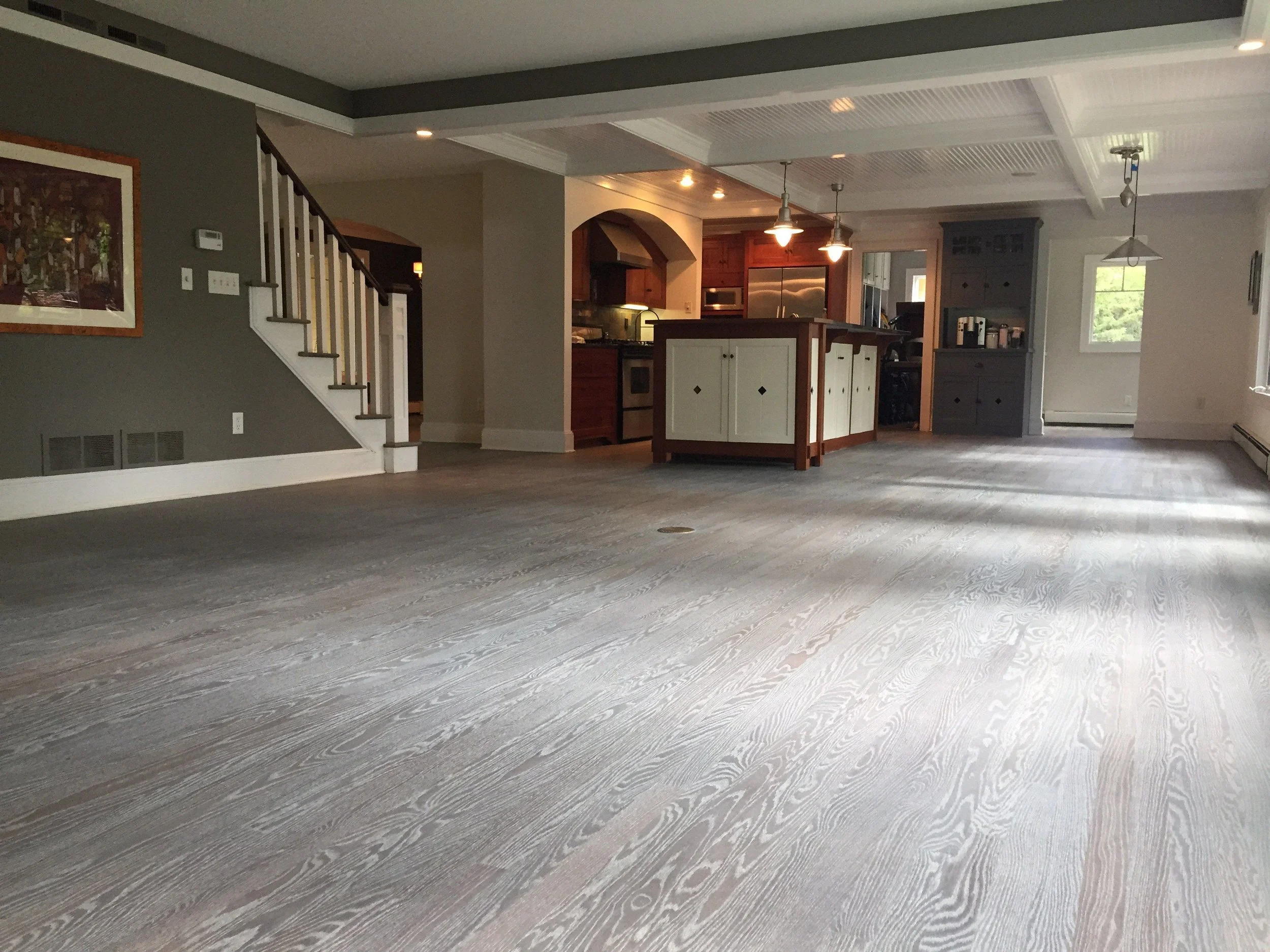 Open-concept living space with gray flooring, kitchen with wooden cabinets and stainless steel appliances, dining area, and large window with natural light.