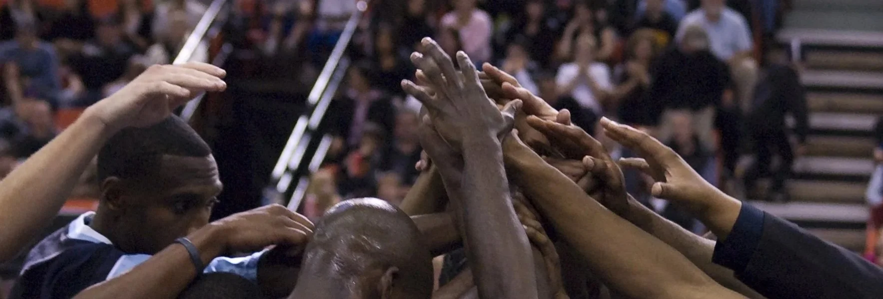 A group of people with their hands stacked together in a celebratory gesture at a sports event.