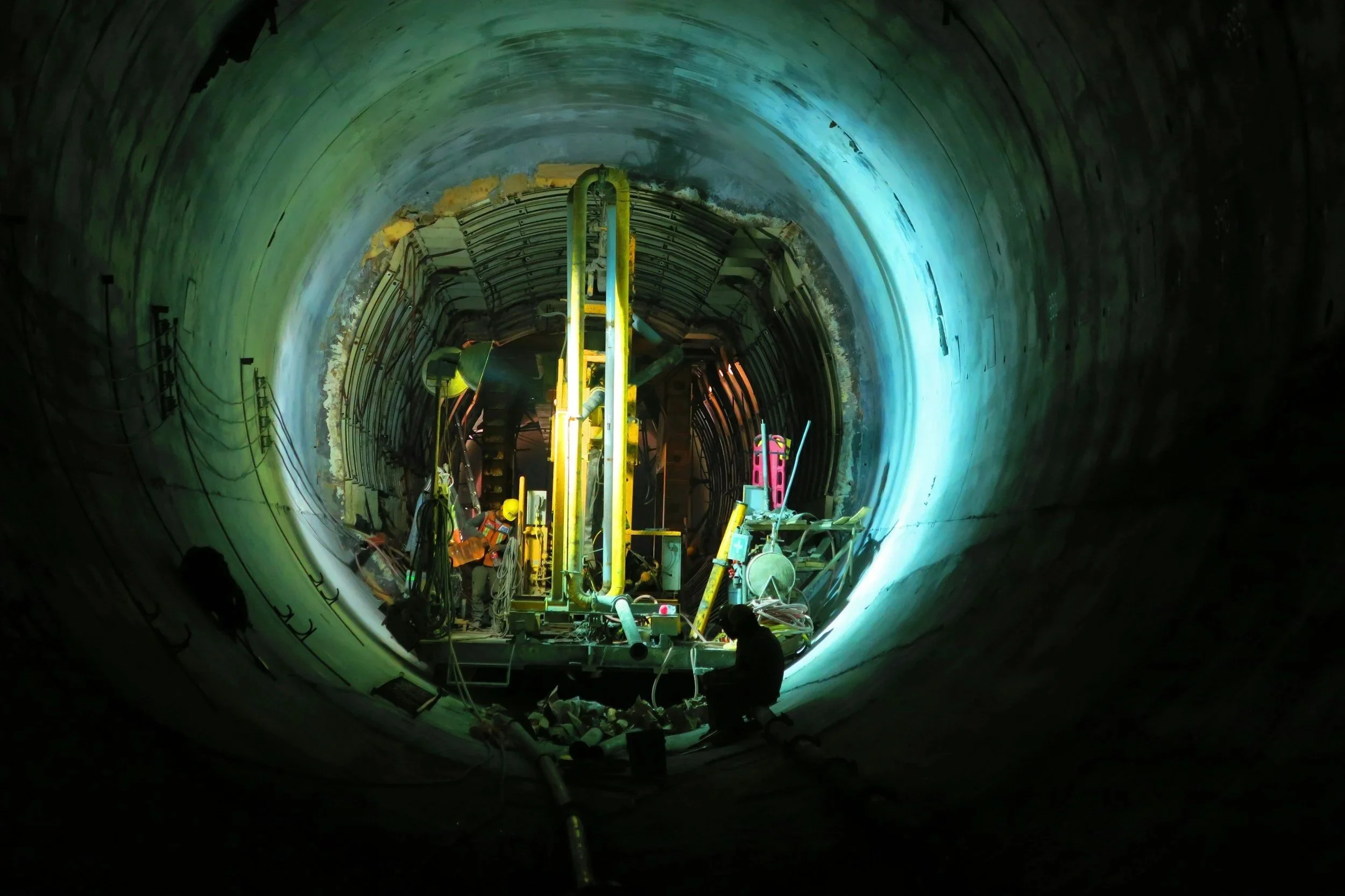 Workers inside a large underground utility tunnel with construction equipment and lighting.