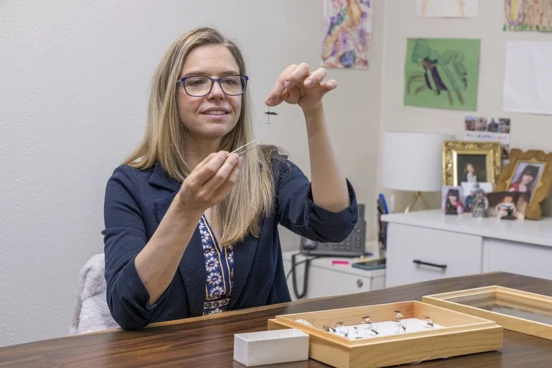 Woman examining jewelry with a magnifying glass at a desk in a home office.