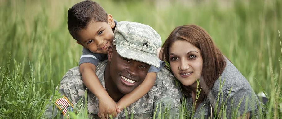 A soldier in uniform lying on grass with a woman and a boy, all smiling and looking at the camera.