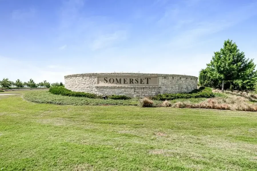Entrance sign for Somerset community with stone wall and greenery, under a blue sky.