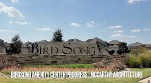Sign for Bird Song Amenity Center under construction in McCarthy Architecture, with a brick wall and a grassy area in front.