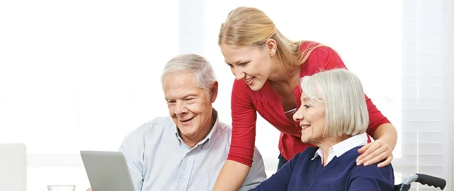A young woman helping an elderly man and woman with a laptop.