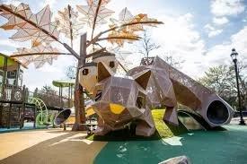 Playground with geometric animal sculpture, trees, and playground equipment in the background under a partly cloudy sky.