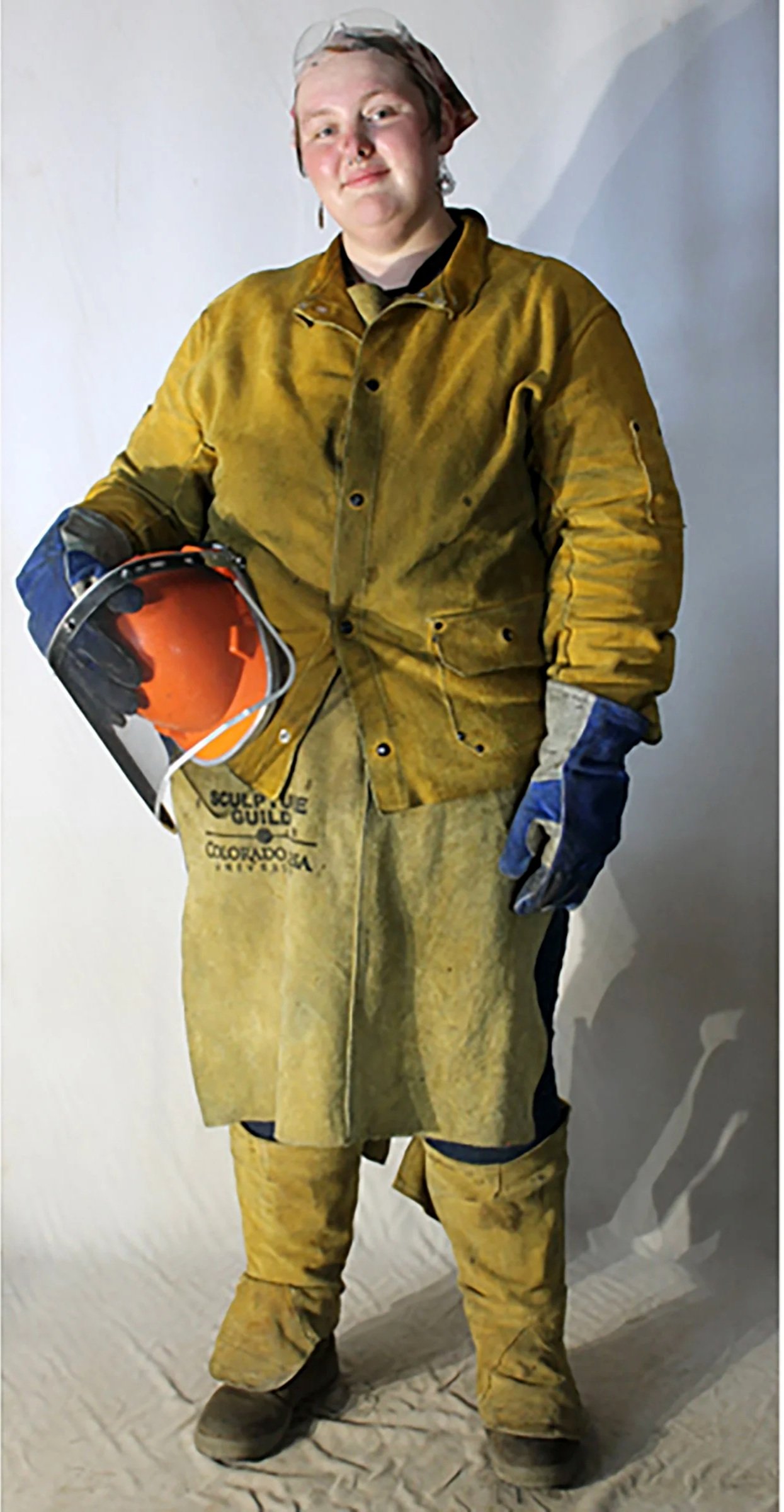 Person dressed in yellow leather protective equipment holding a helmet and wearing gloves.