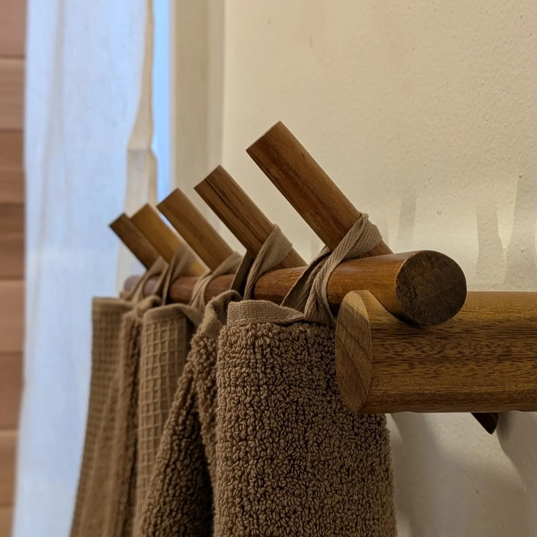 Close-up of wooden hooks on a wooden rack holding beige towels or robes in a bathroom or spa setting.