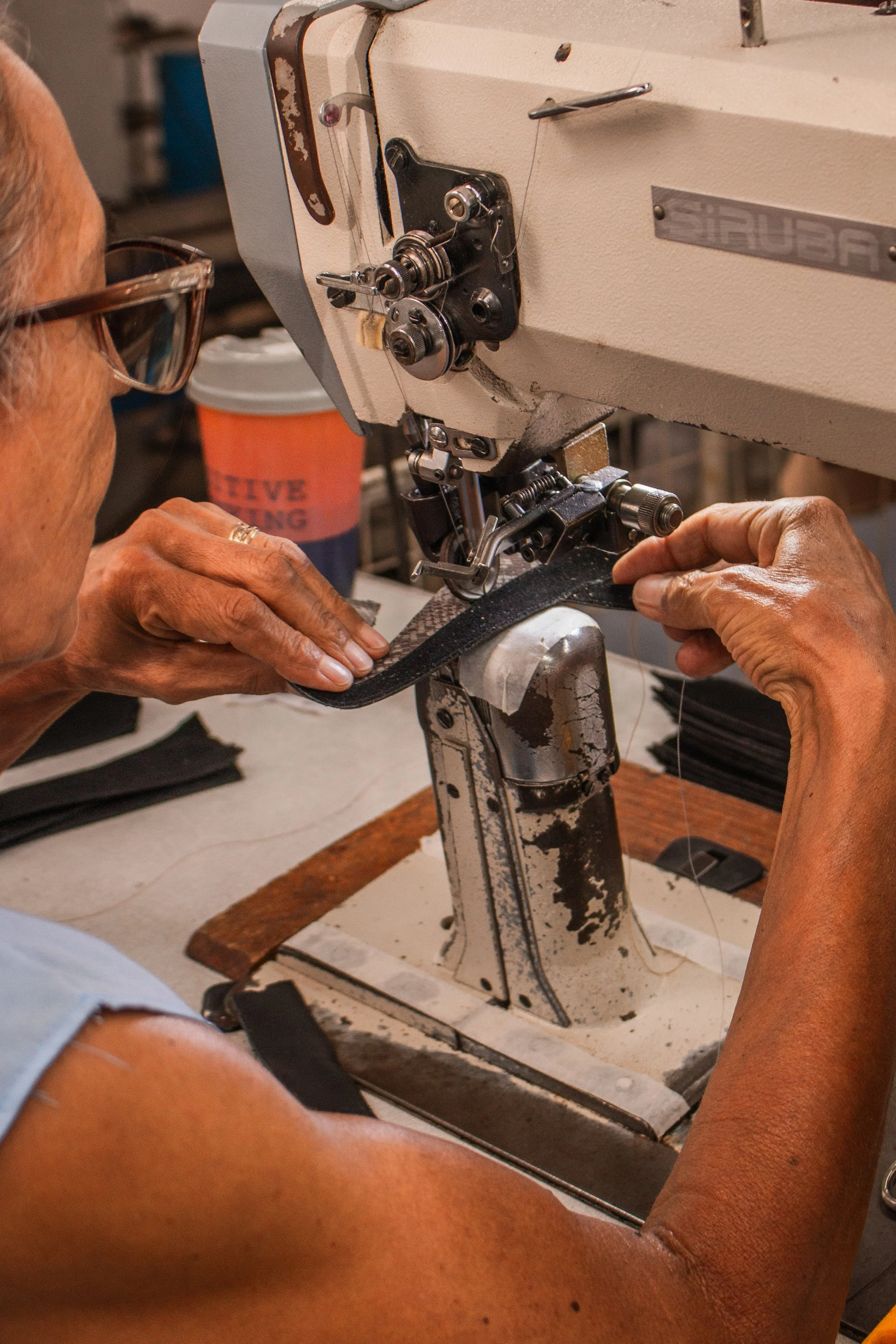 Pessoa costurando uma tira de material rígido em uma máquina de costura industrial.