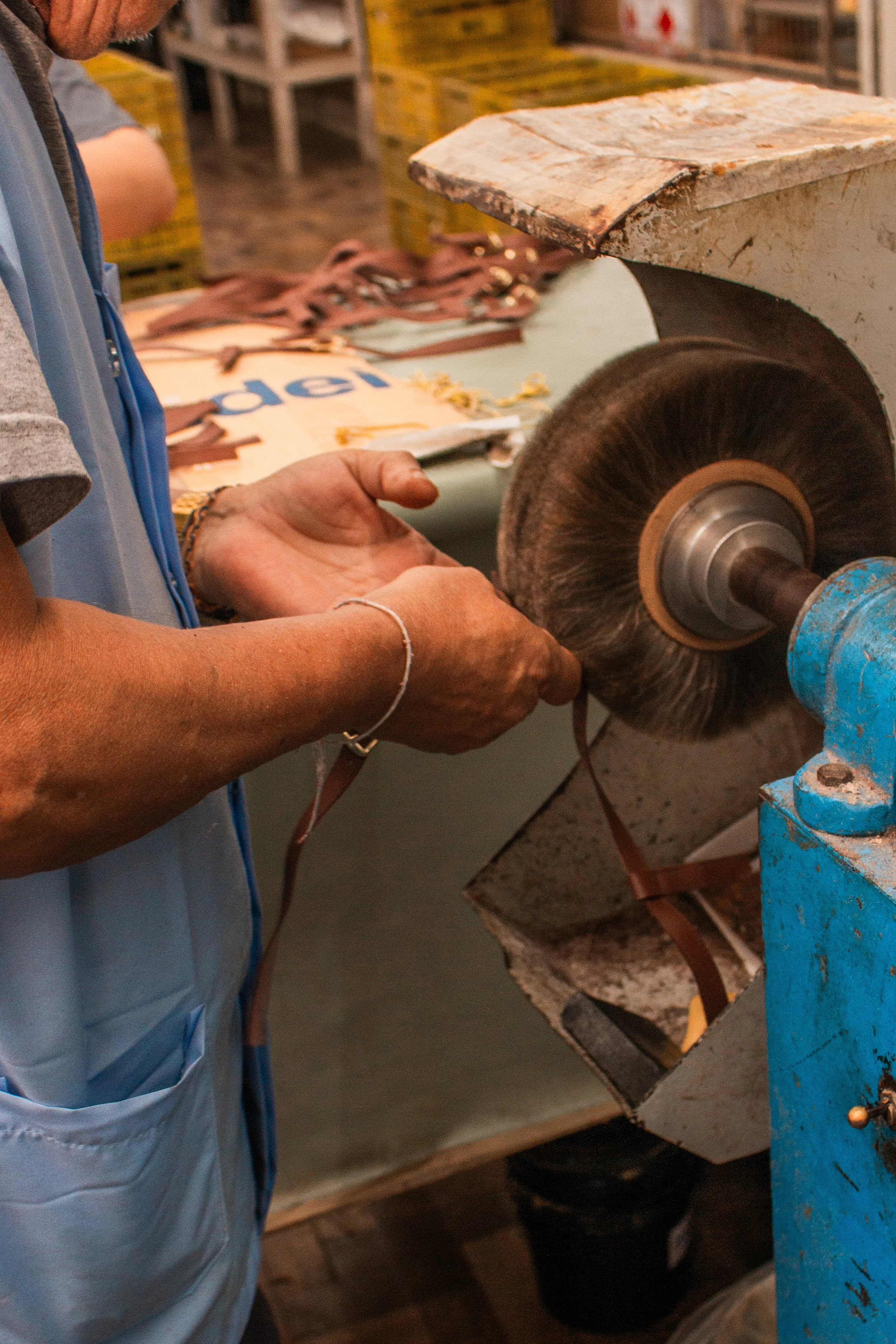 Pessoa manuseando fivela de couro em uma roda de lixadeira em ambiente de produção artesanal.
