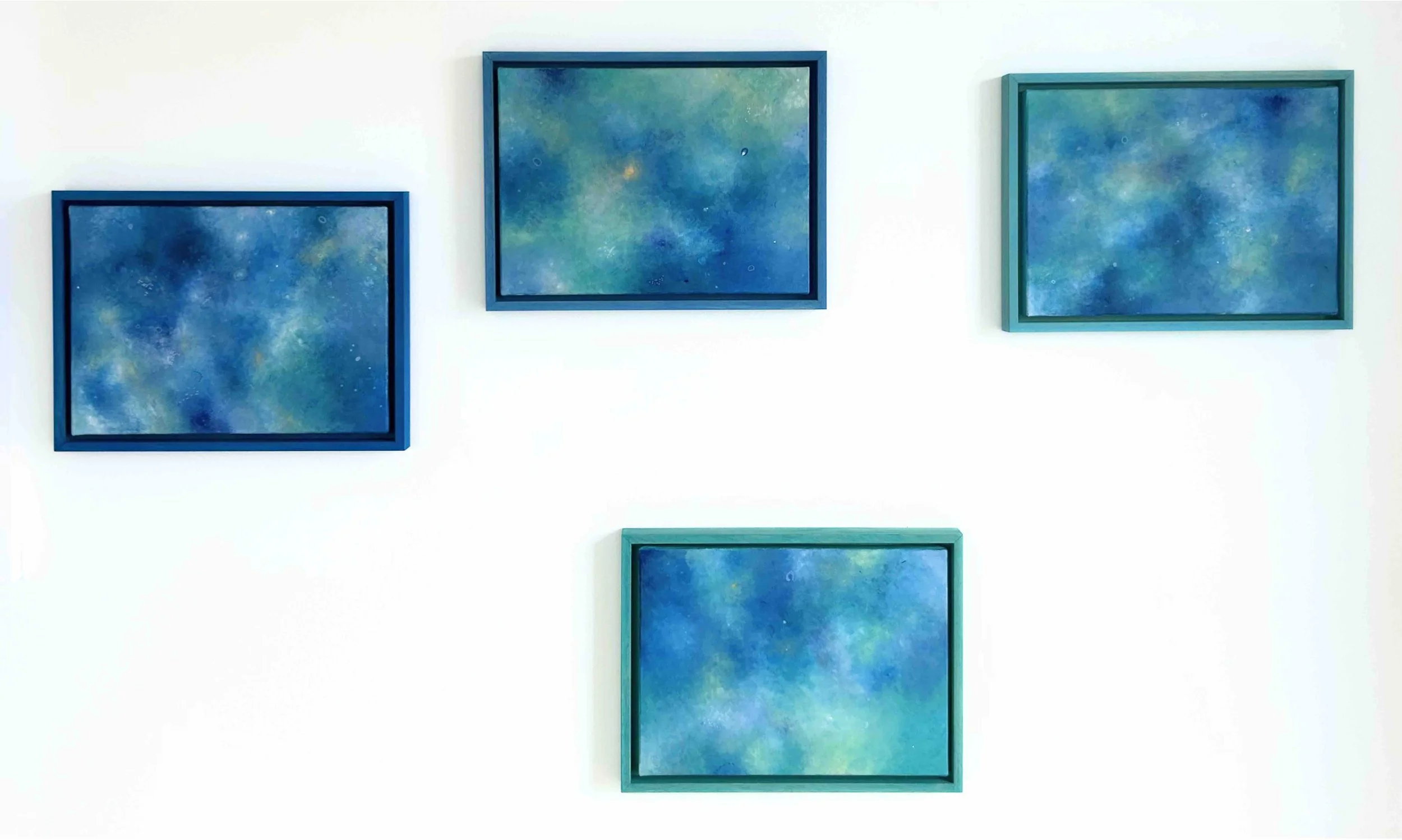 Series of abstract paintings in blue tones, framed and displayed on a white wall