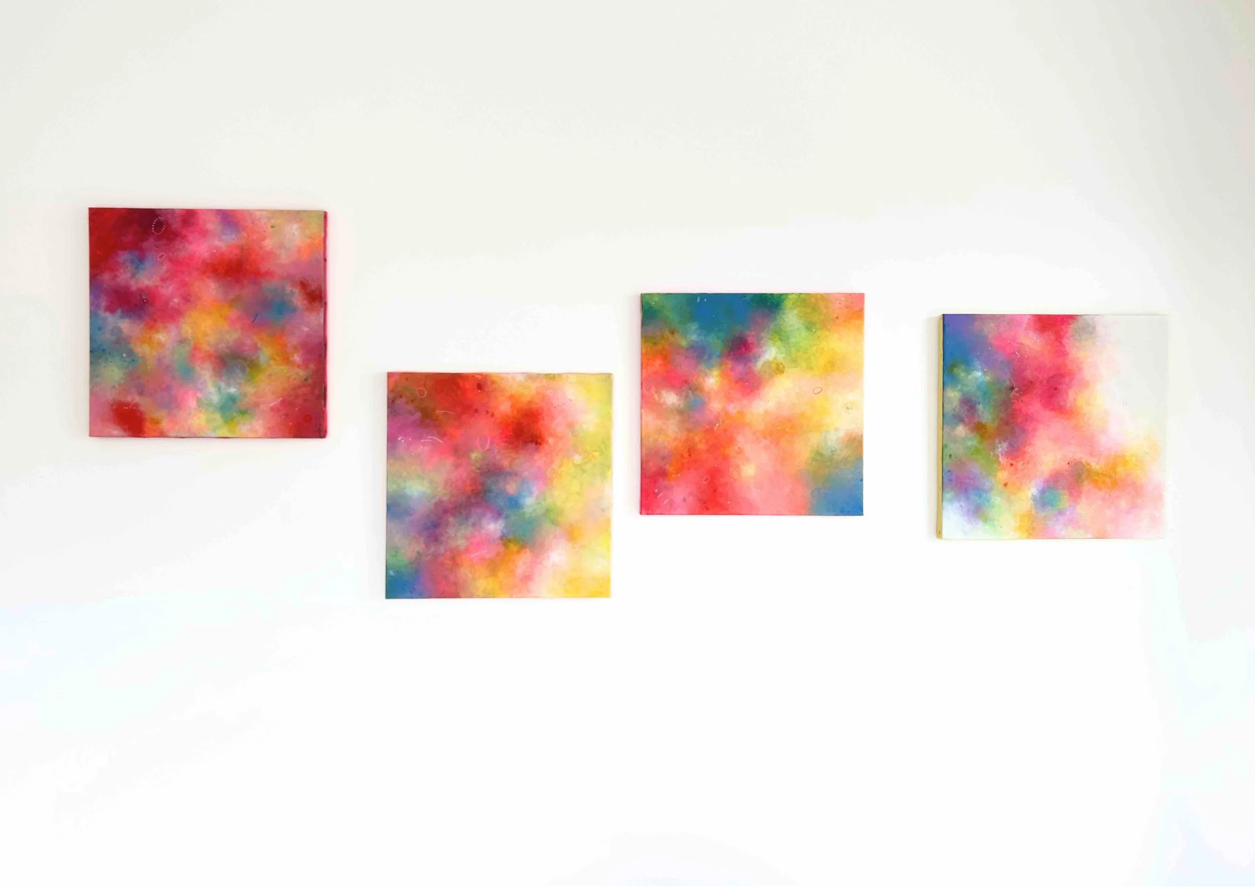 Series of four abstract paintings with soft, colorful gradients displayed on a white wall