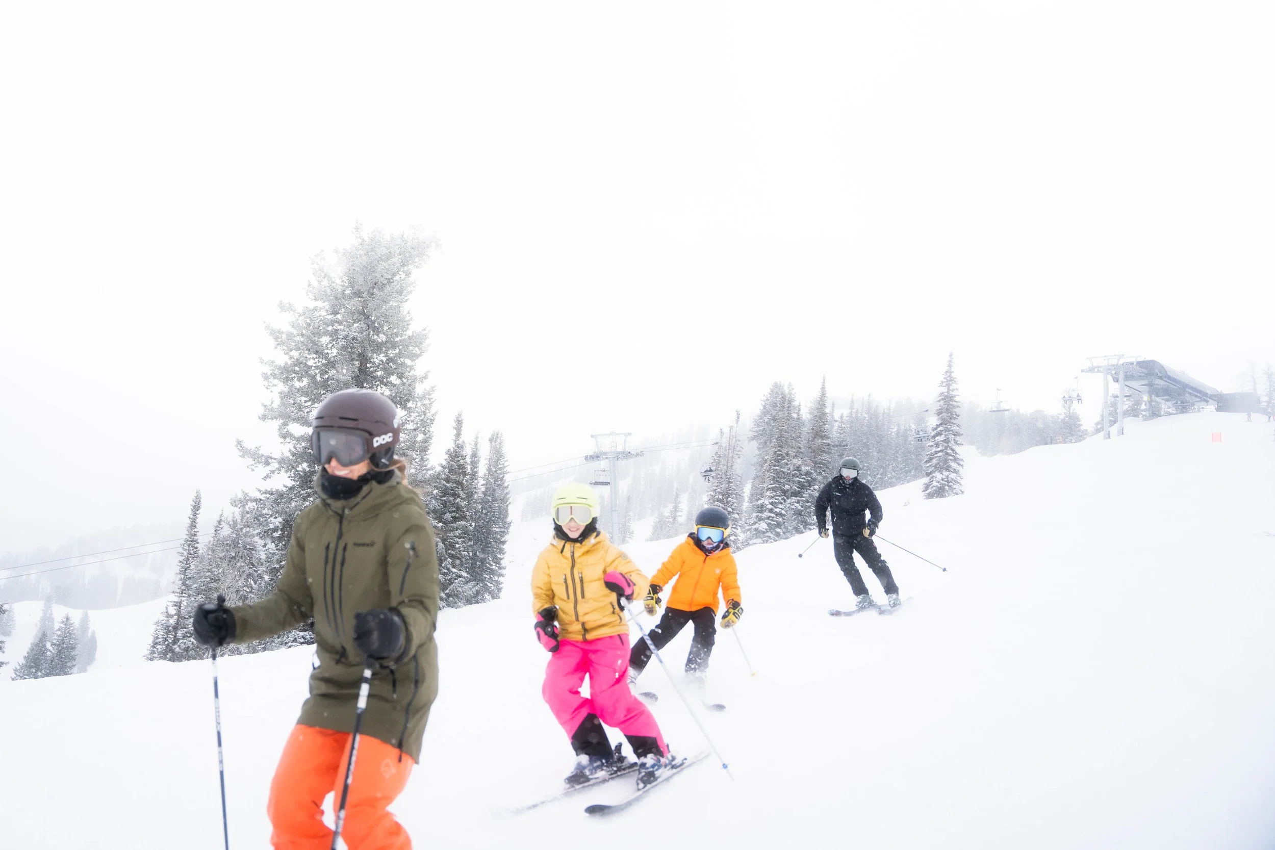 People skiing on a snowy mountainside during daytime with ski lifts and snow-covered trees in the background.