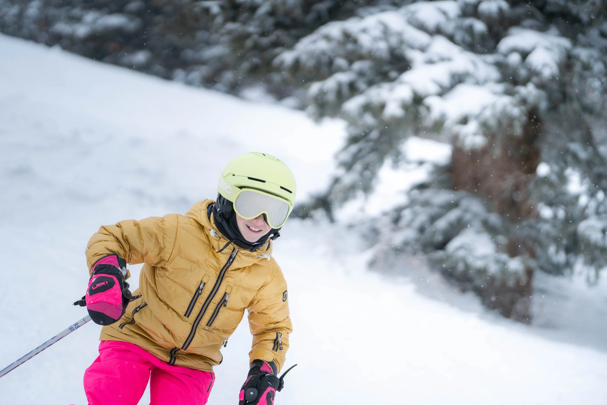 A person skiing in snowy mountains, wearing a yellow jacket, pink pants, a helmet, and goggles.