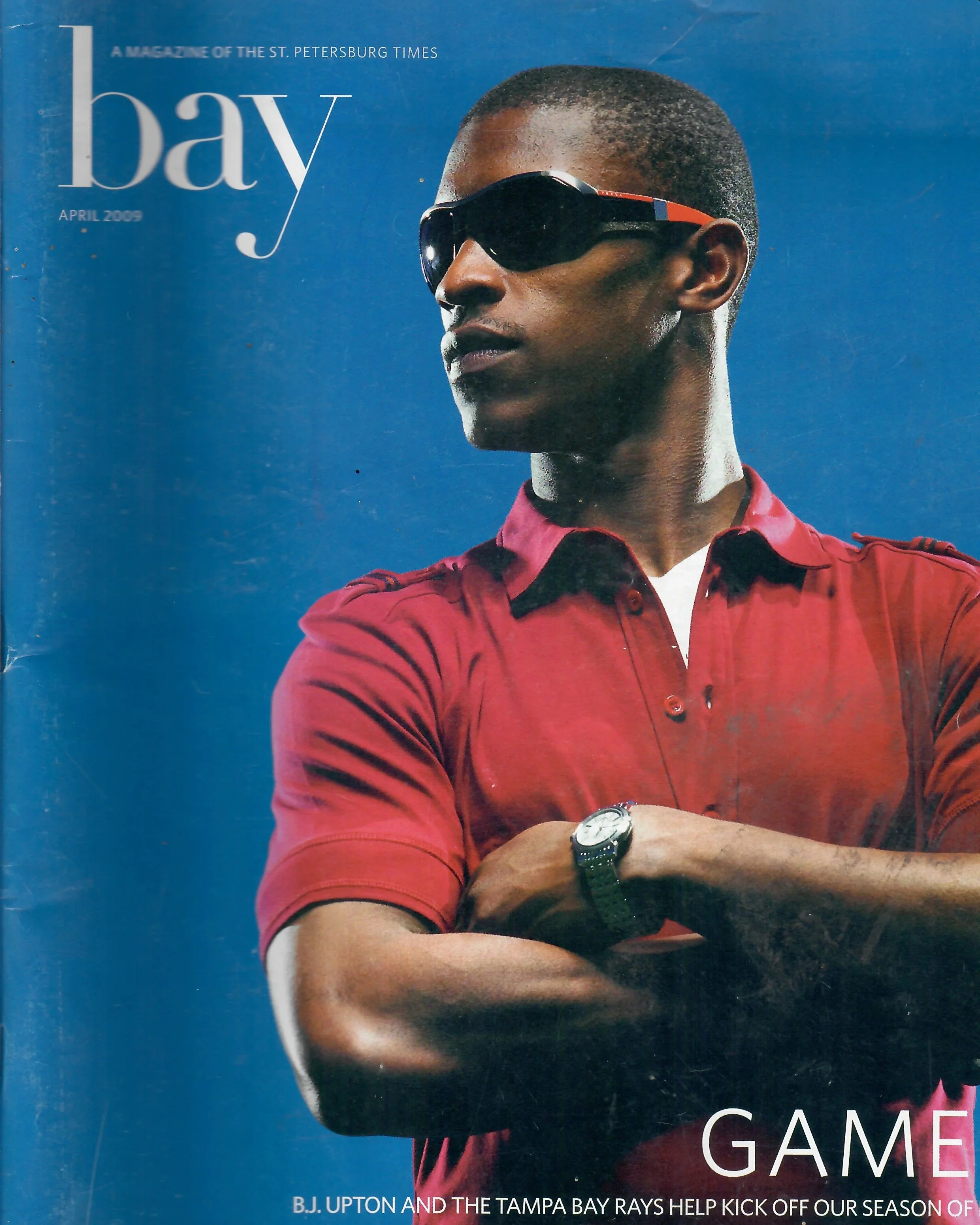 Magazine cover featuring a man in sunglasses and a red collared shirt, with a blue background and the title 'bay' in large white letters.