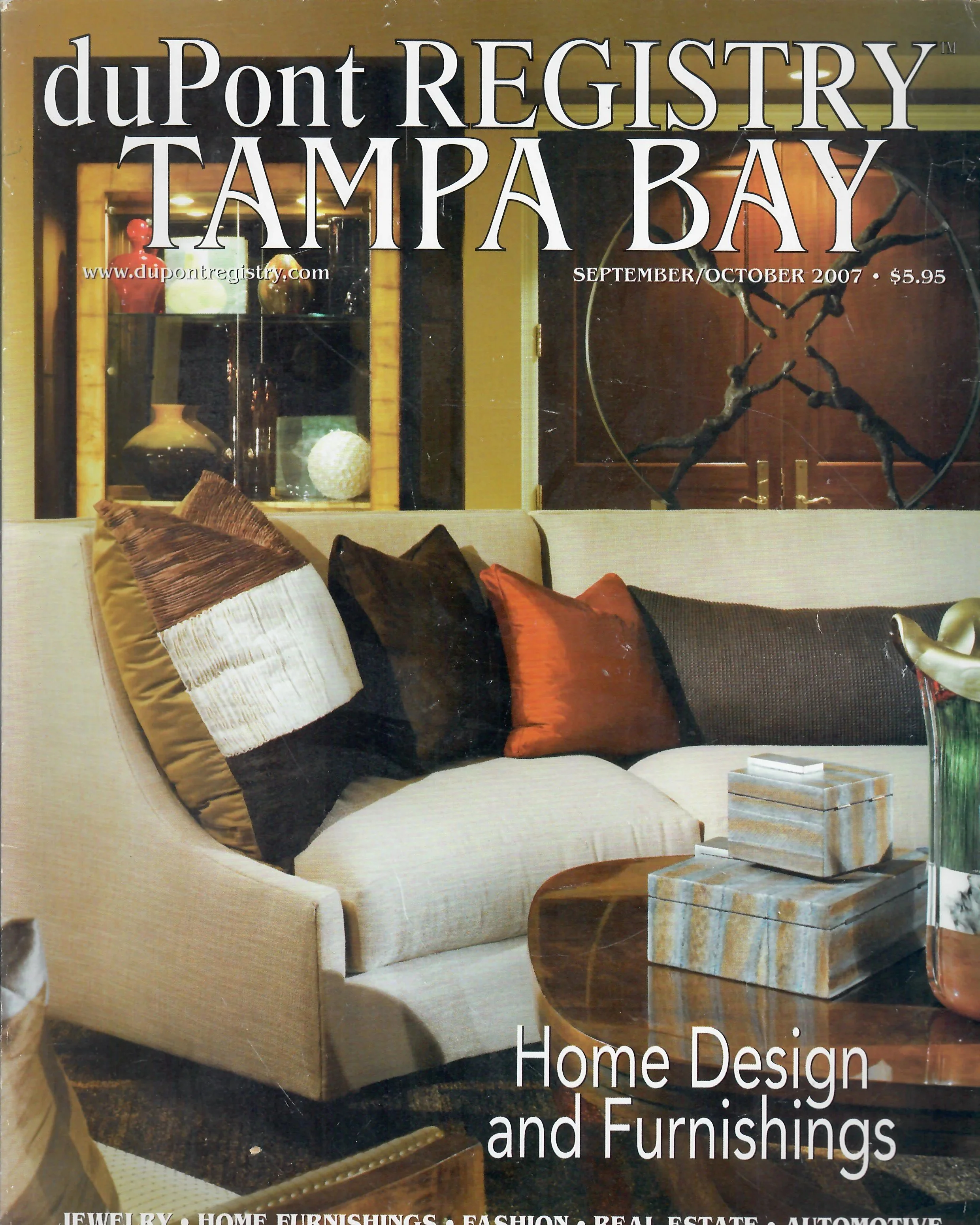 Magazine cover featuring a living room with a beige couch, decorative pillows, a coffee table with a marble top, and a wooden cabinet with vases and ornaments behind the couch. The cover title includes 'duPont REGISTRY TAMPA BAY' and mentions home de