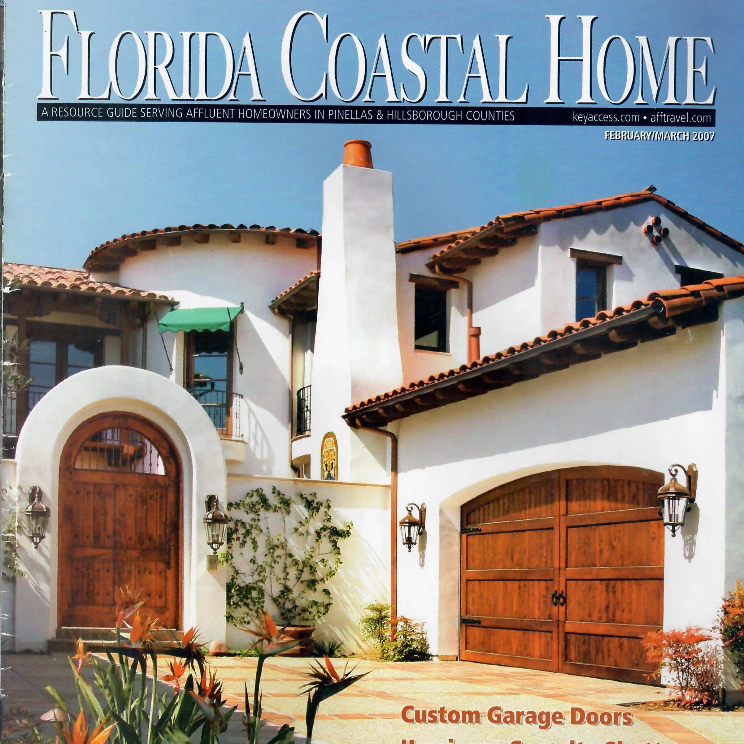 A glossy magazine cover titled "Florida Coastal Home" features the exterior of a Mediterranean-style house with white stucco walls, orange clay tile roof, arched wooden garage doors, and a courtyard with potted plants, lantern-style light fixtures, a