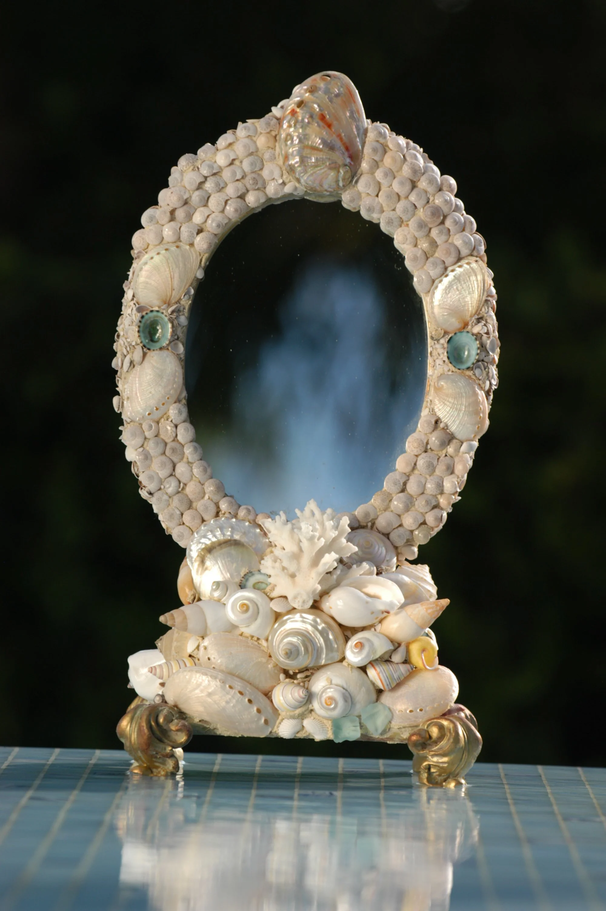A mirror decorated with seashells and small sea-themed ornaments, standing on ornate gold-colored legs.